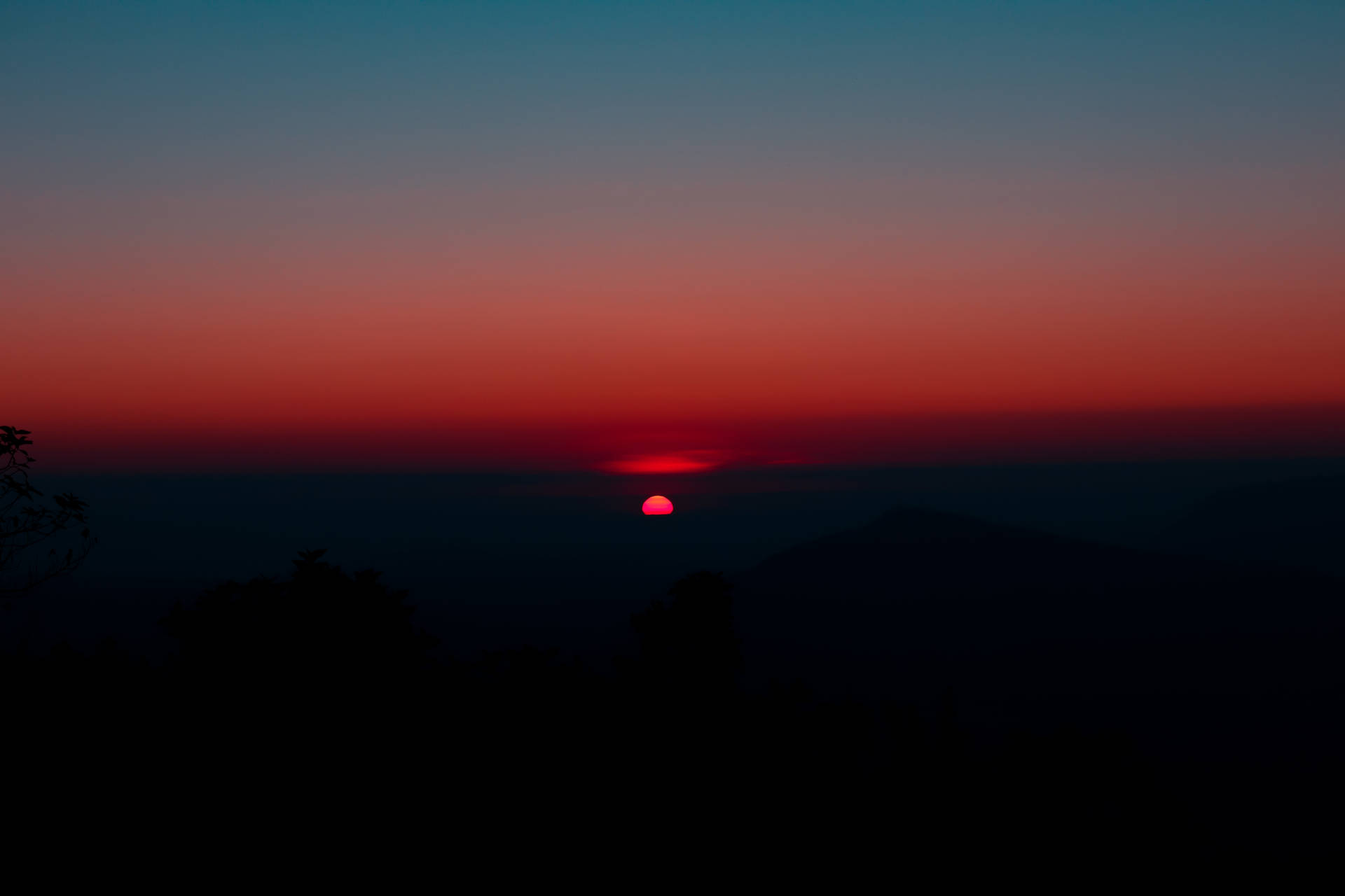 在漸變色的天空中，一輪紅日落在山巒輪廓之後。 — Lofi 壁紙