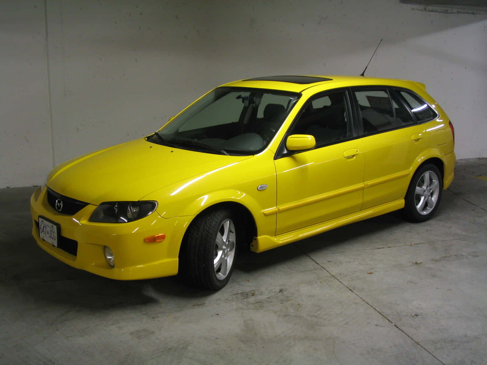 Mazda Protege 桌布 壁紙 — 一輛鮮黃色的Mazda 3掀背車停放在混凝土車庫內，牆壁和地板均為素色。