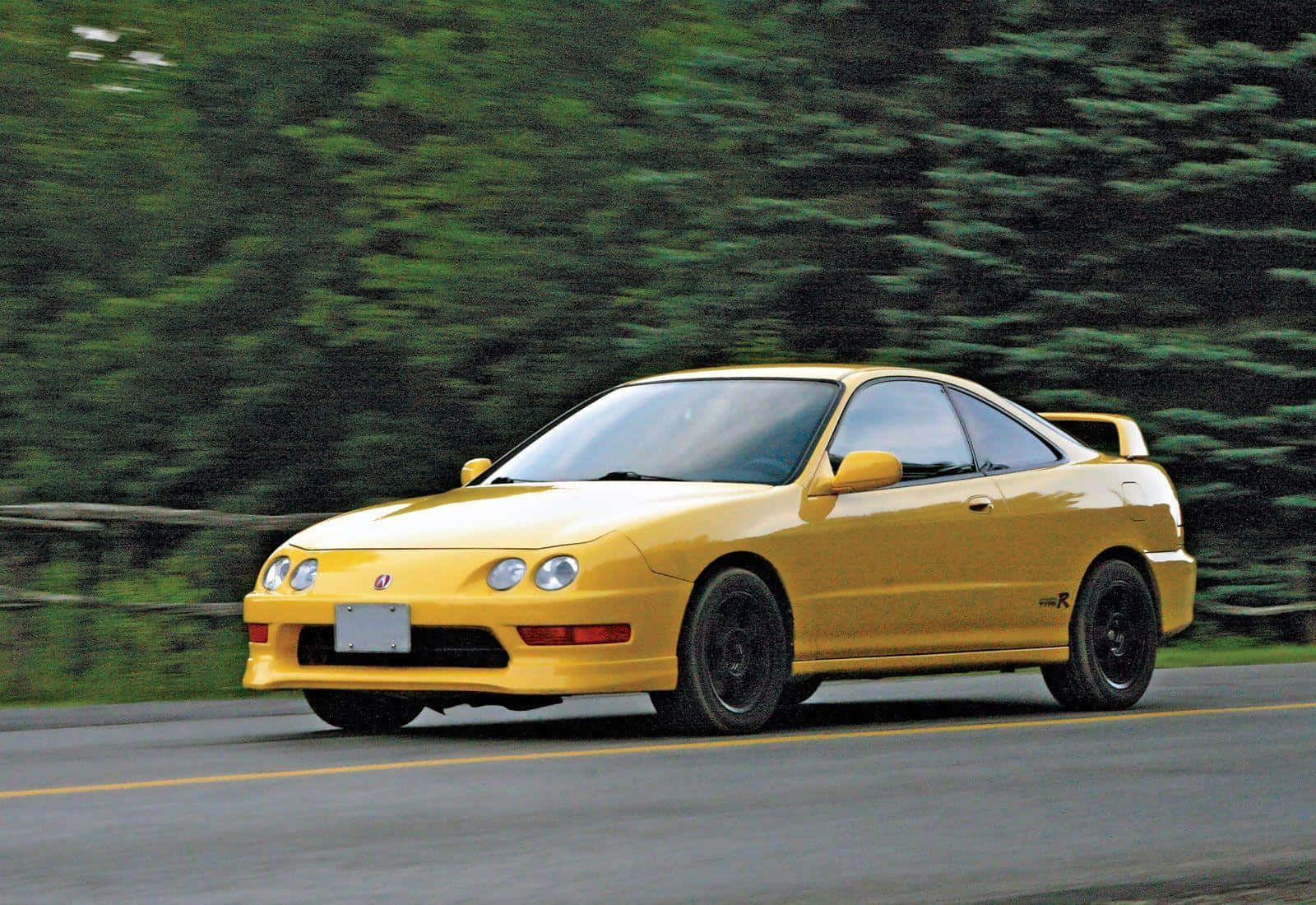 Acura Integra 桌布 壁紙 — 一輛充滿活力的黃色跑車在道路上疾馳，背景是模糊的綠色樹木。
