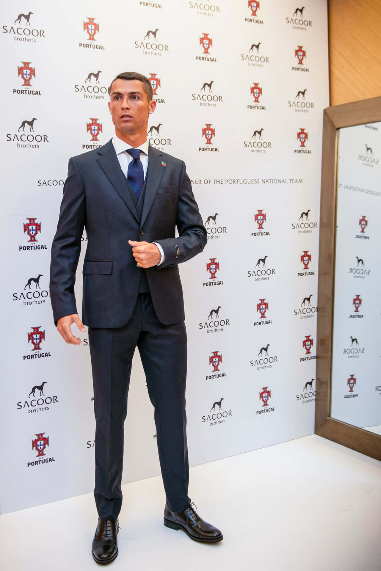  壁紙 — Cristiano Ronaldo 的蠟像身穿筆挺海軍藍西裝，站在印有葡萄牙和 Sacoor Brothers 標誌的品牌背景前。
