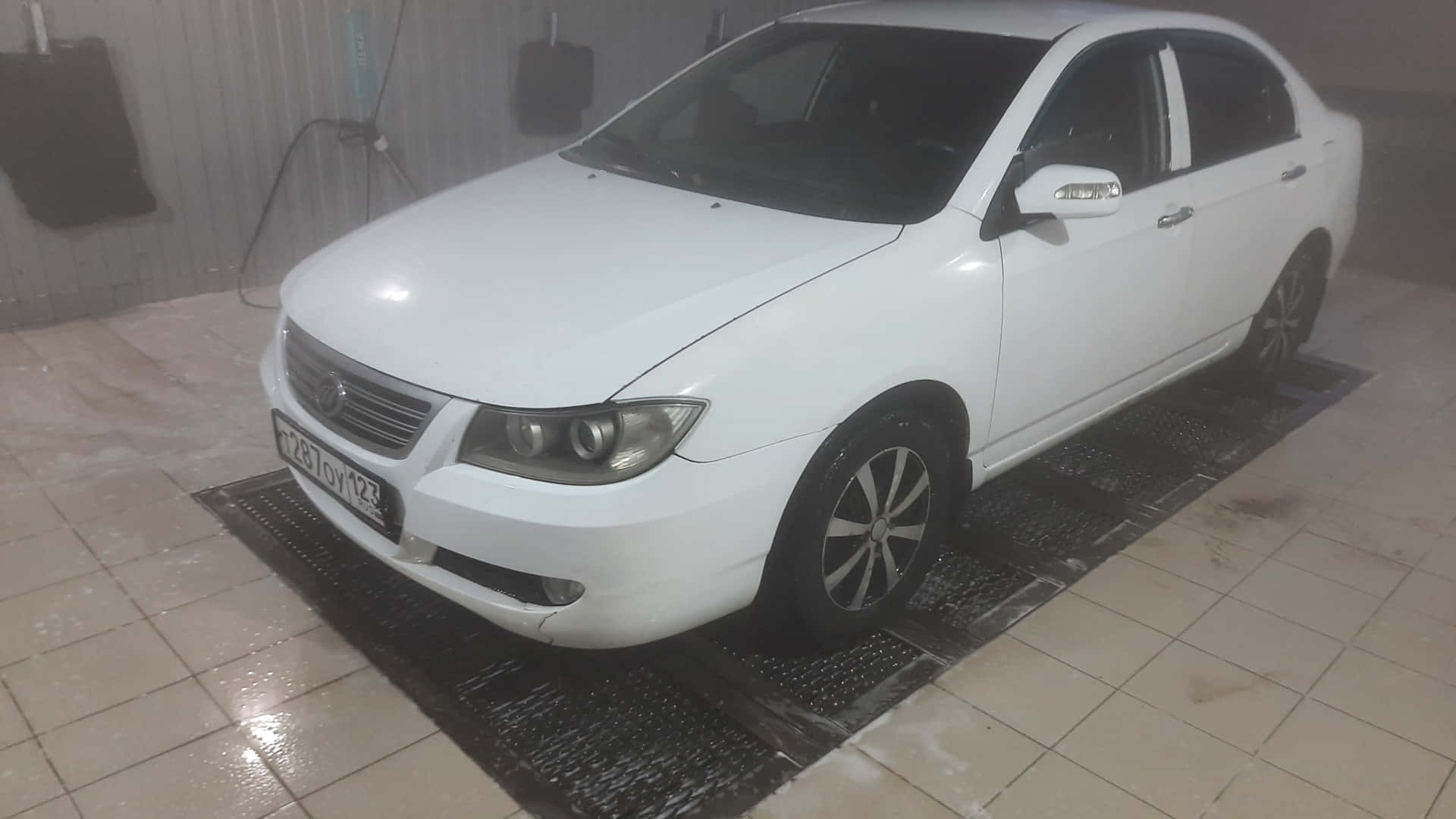 Lifan 620 桌布 壁紙 — 一輛白色轎車正在室內洗車場的濕格柵上被清洗，周圍有蒸汽升起。