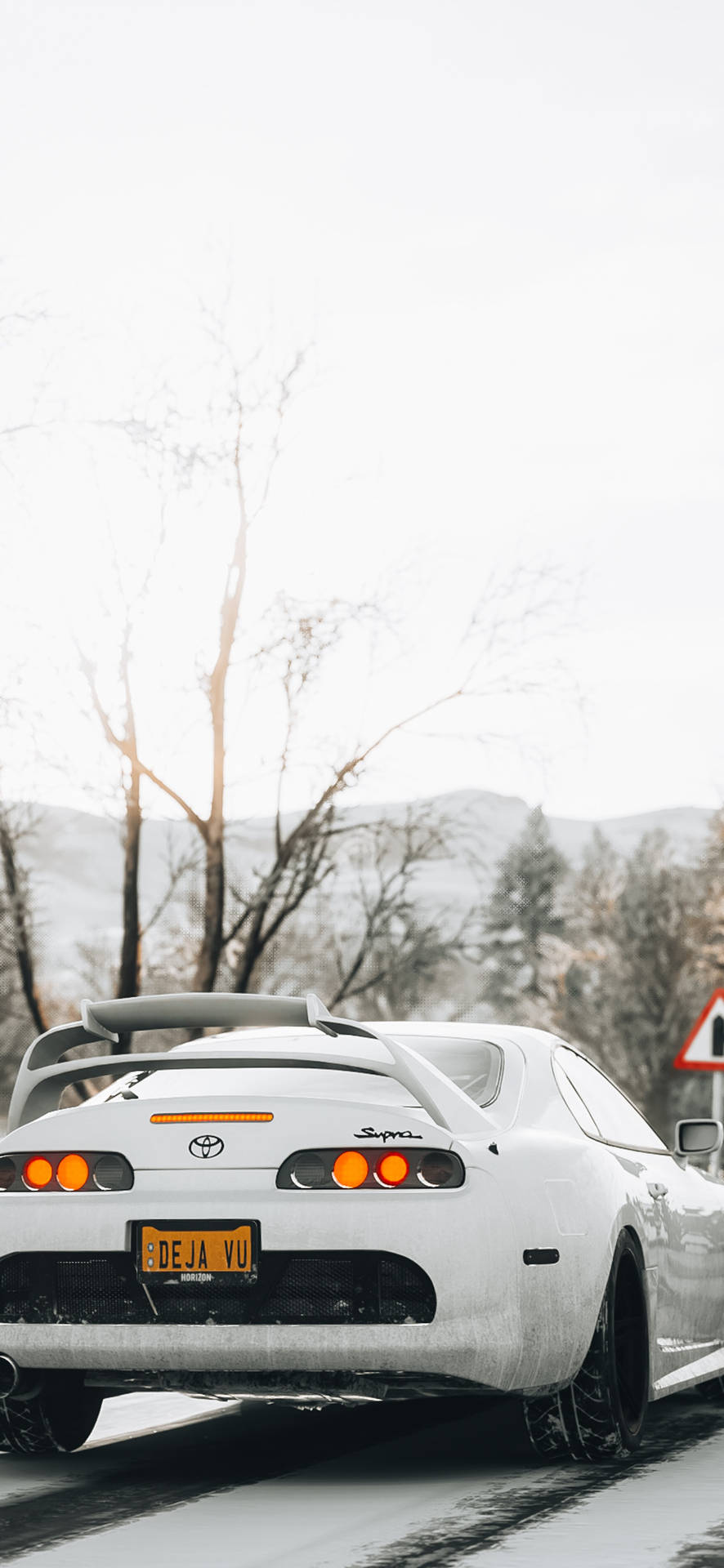 白色豐田Supra在積雪道路上飄移，光禿樹木和山脈在日落時分。 — Toyota Supra 壁紙