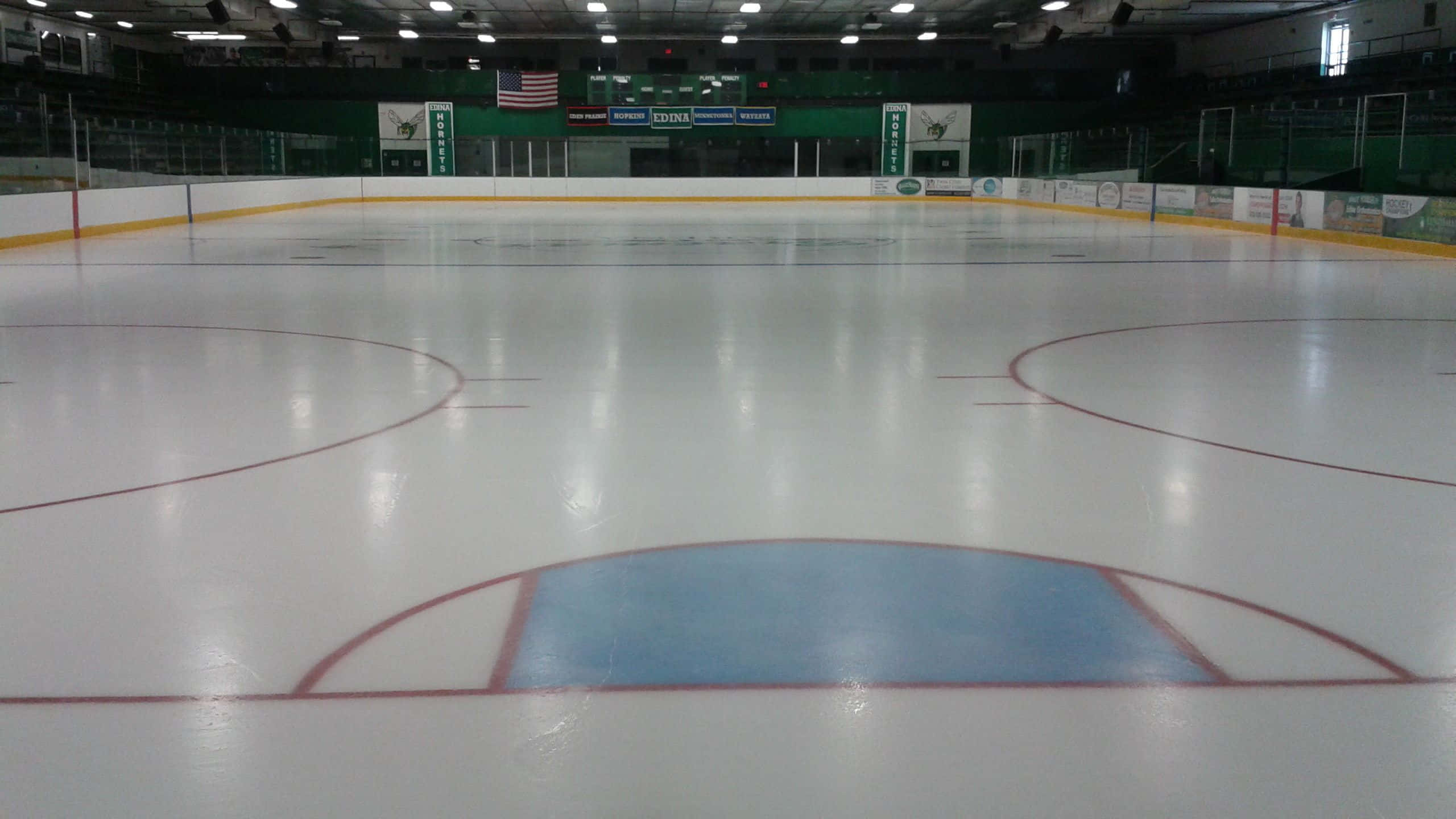 Ice Rink 桌布 壁紙 — 一個寬闊空無一人的冰球場，有紅色標記和藍色中圈，上方有明亮的頂燈。