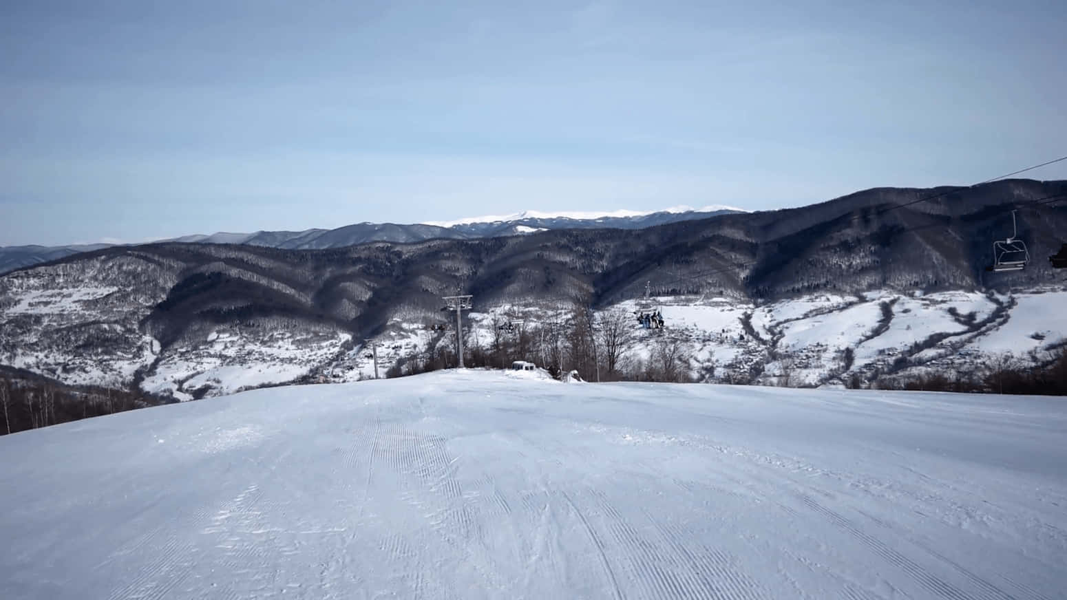 冬季的雪地滑雪道，設有纜車和森林覆蓋的山脈。 — 4K 壁紙