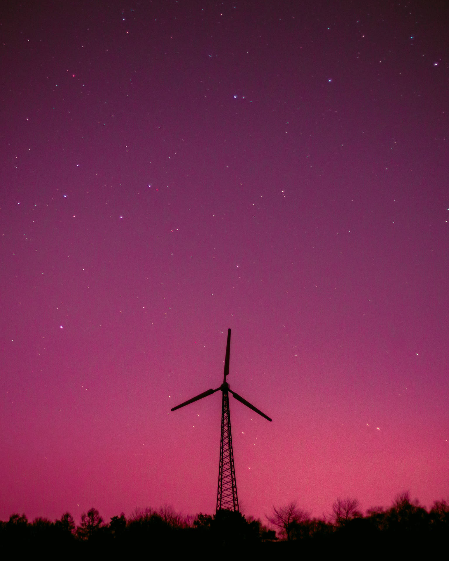 風力渦輪機的剪影，在繁星點點的紫色夜空下，下方有樹木。 — iPhone 13 Pro Max 壁紙