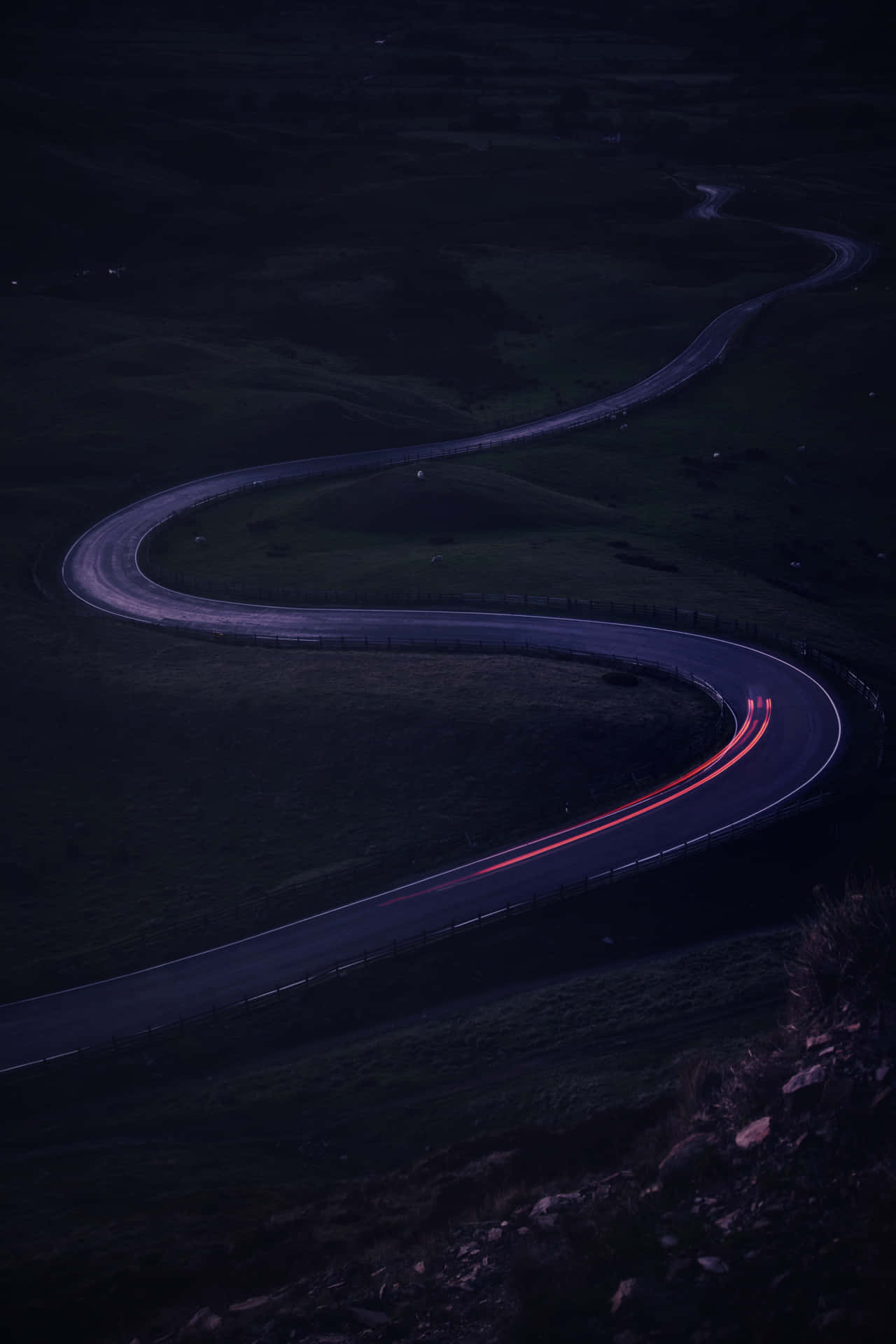 黃昏時分彎曲的道路，行駛車輛留下的紅色光跡。 — iPhone 11 Pro Max 壁紙