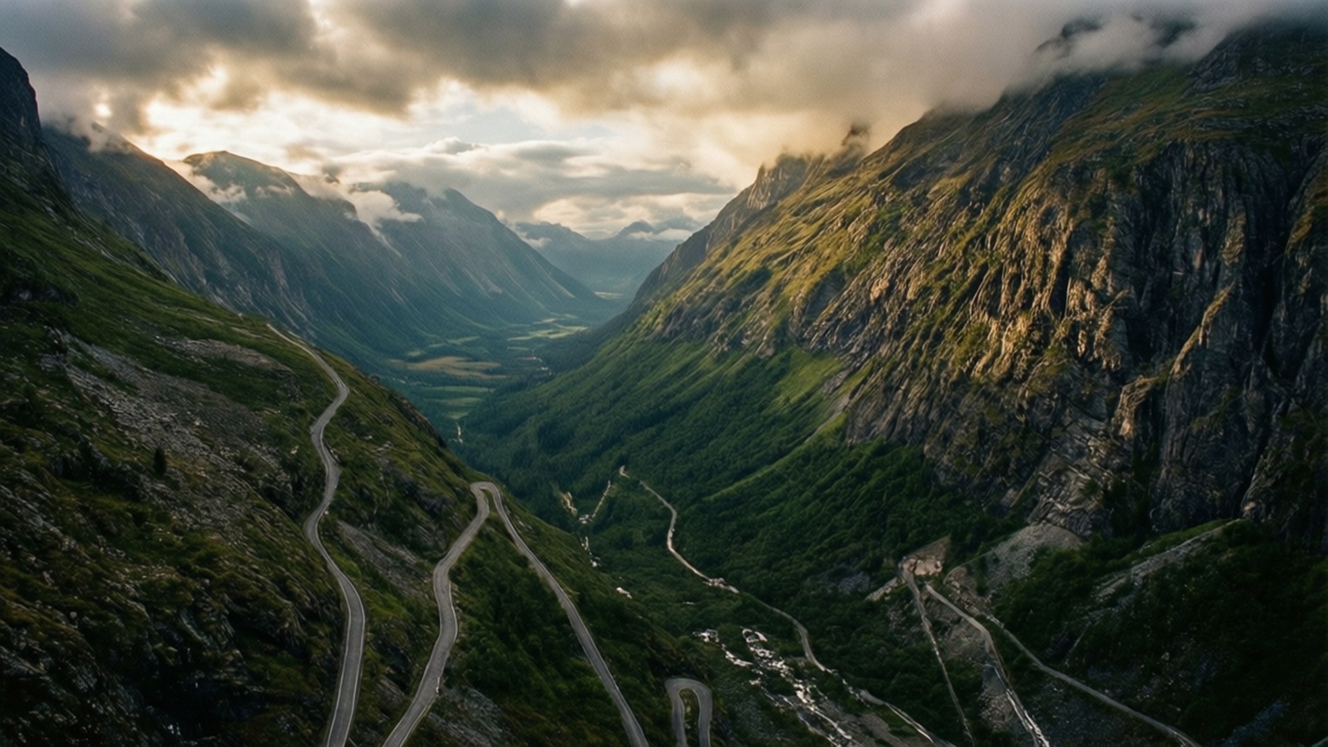 Mountain Pass 壁紙 — 一條蜿蜒的山路穿過深綠色的山谷，兩旁是陡峭的岩石懸崖，天空陰雲密佈，氣氛戲劇化。