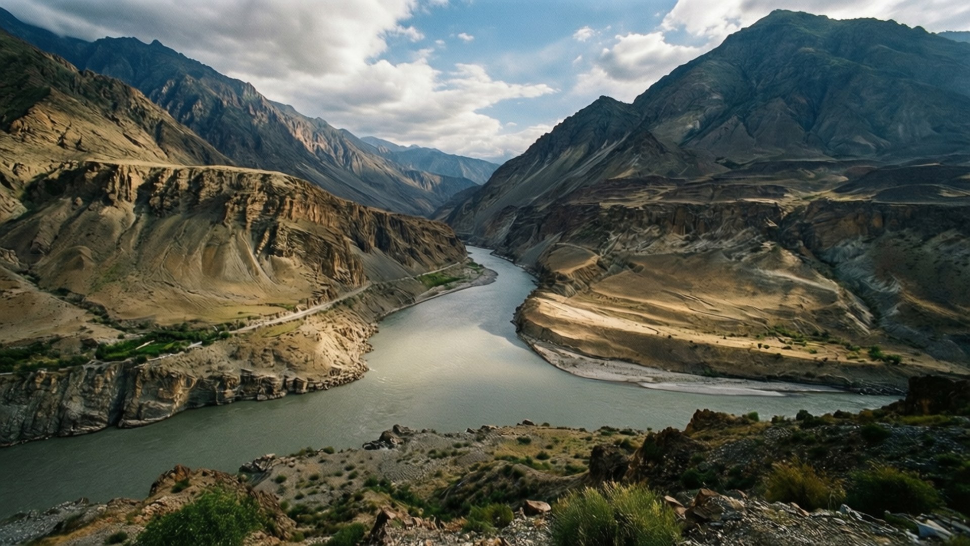 Indus River Valley 壁紙 — 一條蜿蜒的河流穿過崎嶇的峽谷，兩旁是陡峭的岩石山脈，天空部分多雲。