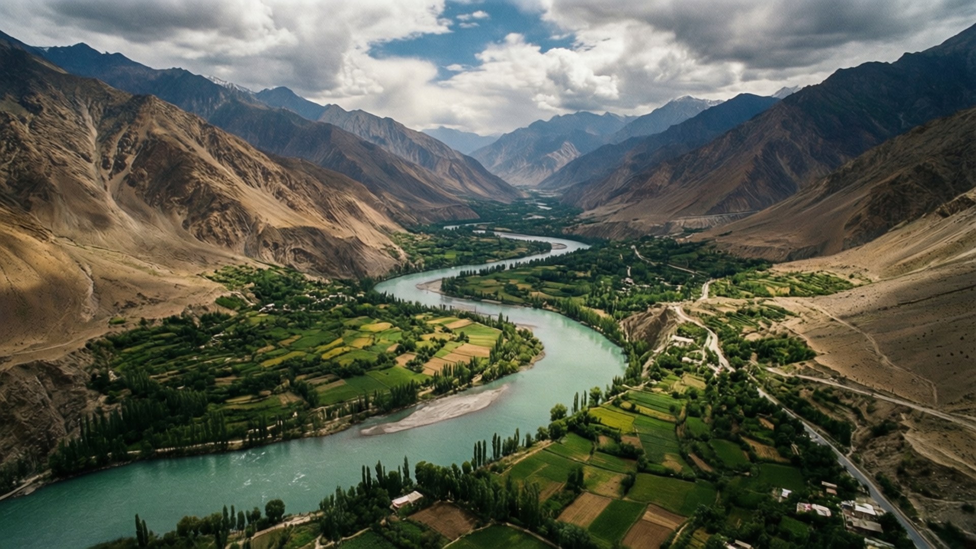 Panjshir Valley Aerial 壁紙 — 一條蜿蜒的綠松石河流穿過鬱鬱蔥蔥的綠色山谷，兩側是崎嶇的棕色山脈，天空多雲，景象壯觀。