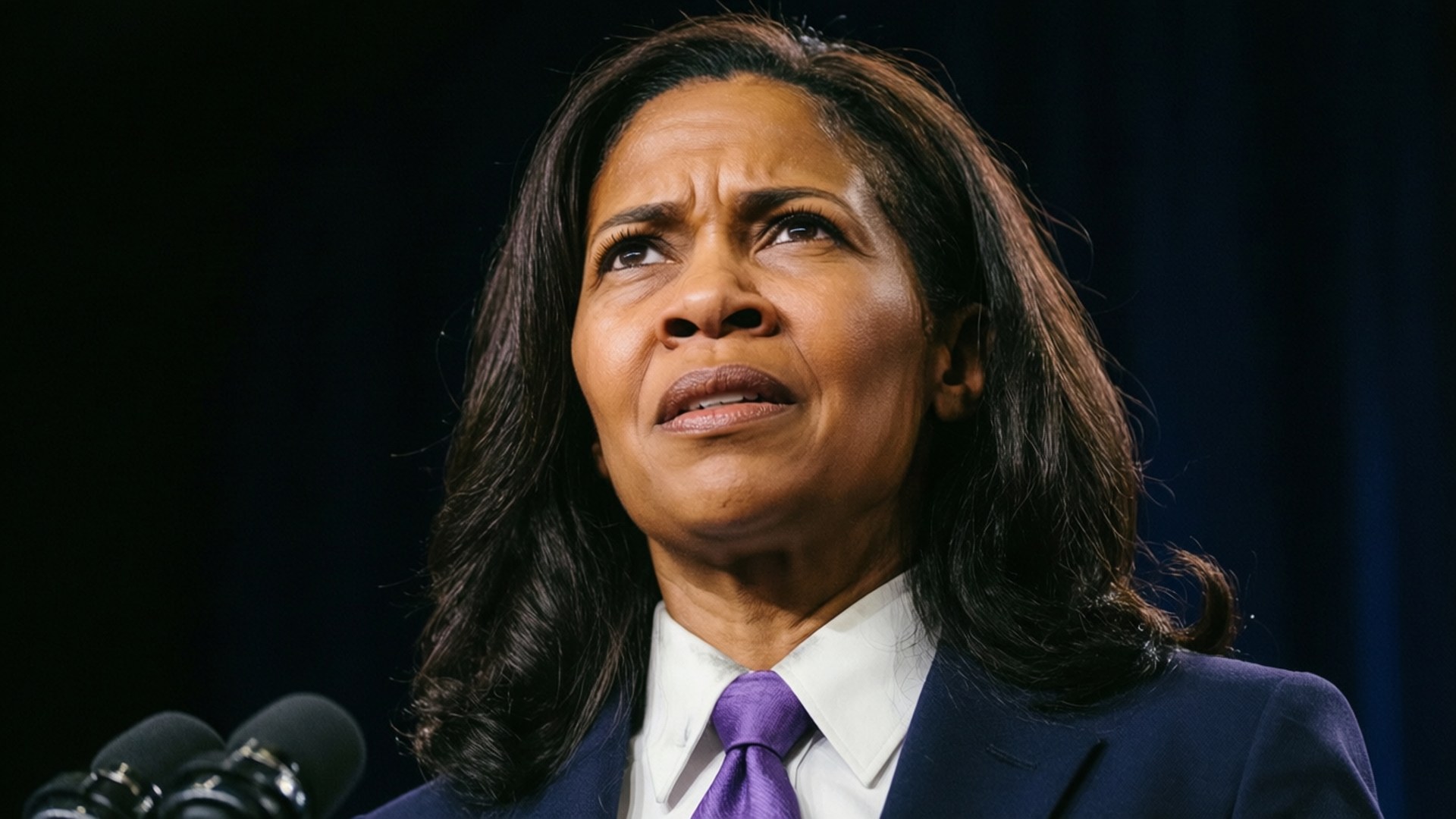 Determined Look 壁紙 — 一位身穿深色西裝和紫色領帶的女性，在深藍色窗簾背景下，帶著憂慮的表情向上看。