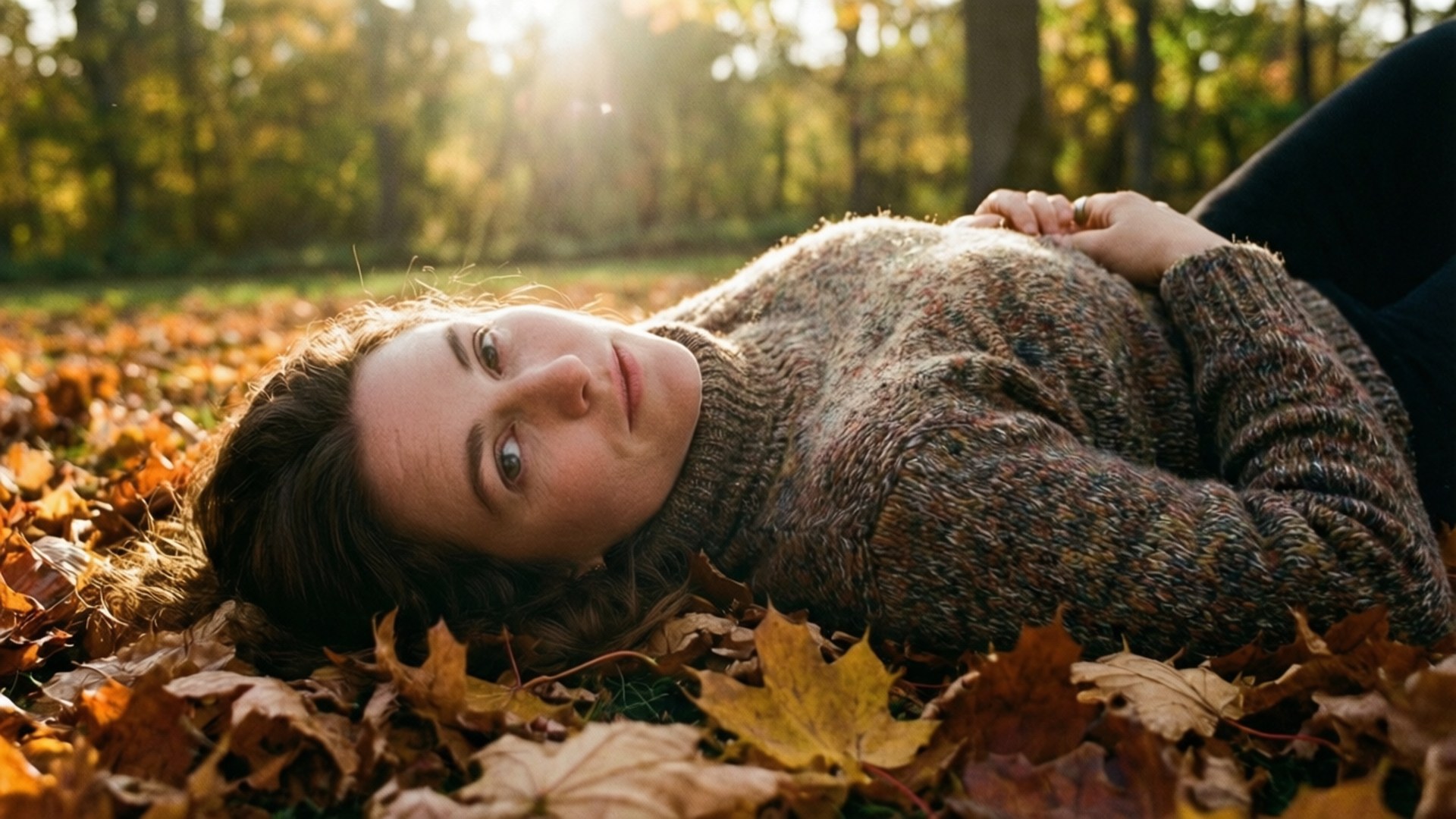 Autumn Serenity 壁紙 — 一位穿著質感毛衣的女性躺在金色秋葉中，陽光透過她身後的樹木灑落。