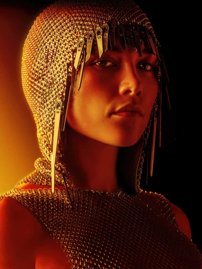  壁紙 — 一位身穿金色鎖子甲和金屬流蘇的女性，在黑暗背景下溫暖的電影燈光中閃耀。
