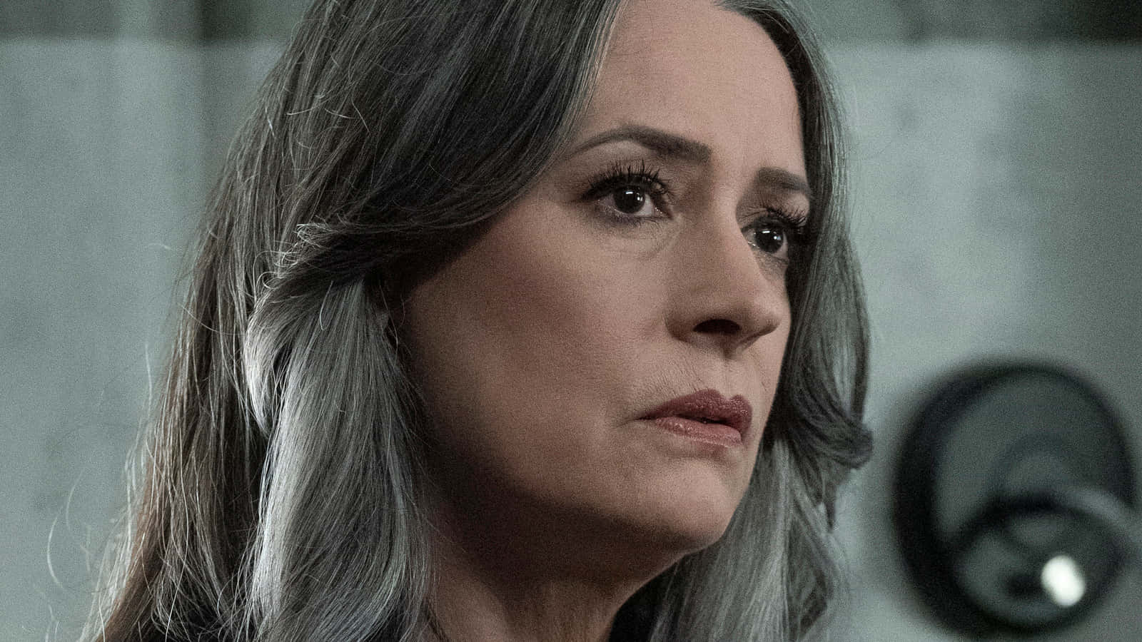 paget brewster 桌布 壁紙 — 一位灰髮女性在附近有監視器的昏暗混凝土房間裏若有所思地凝視著。