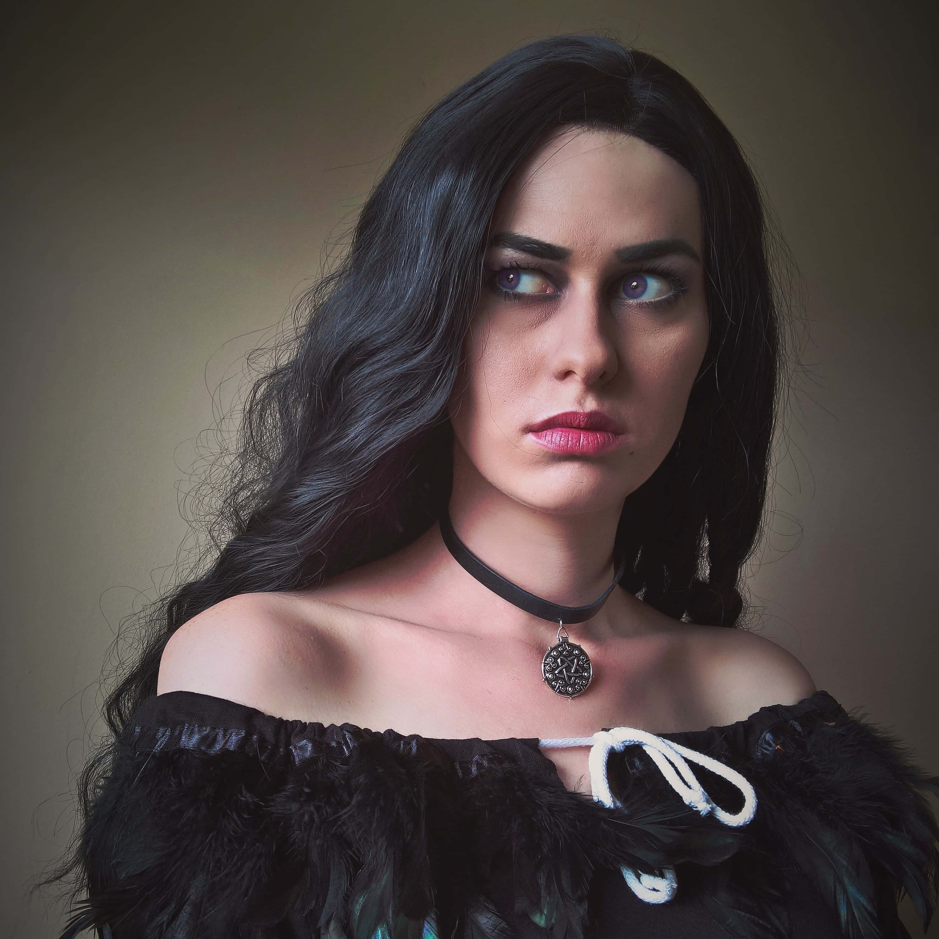 Yennefer 桌布 壁紙 — 一位擁有長黑髮和引人注目的眼睛的女性，在柔和背景前穿著黑色羽毛上衣和頸鏈。