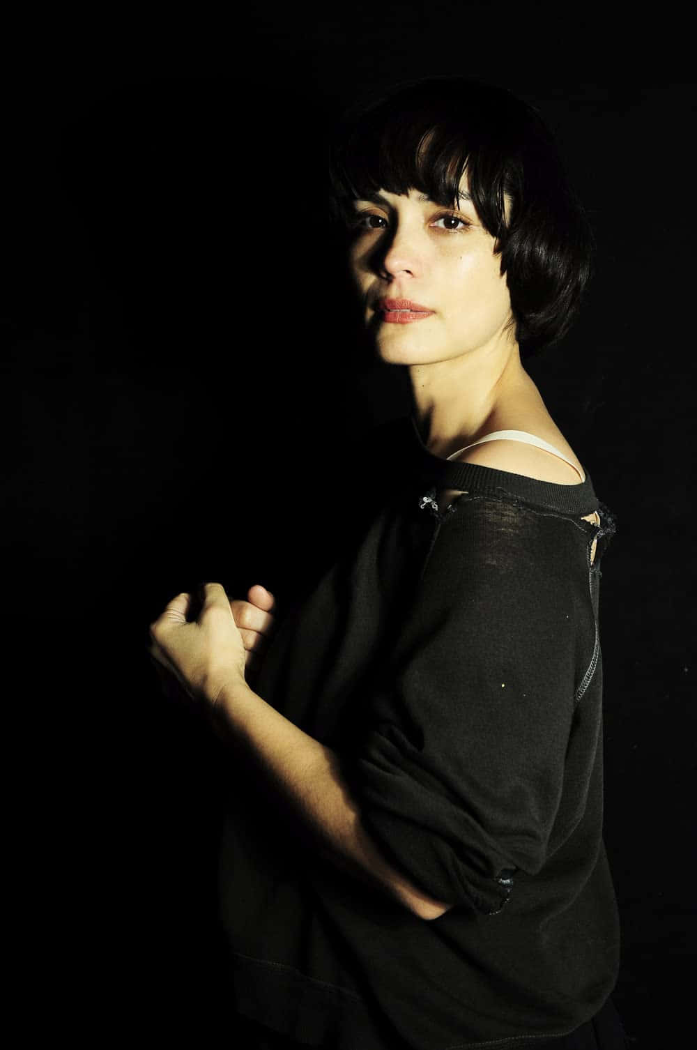 Shannyn Sossamon 桌布 壁紙 — 一位短黑髮女性站在陰影的攝影棚燈光中，她的臉在黑色背景下柔和地照亮。