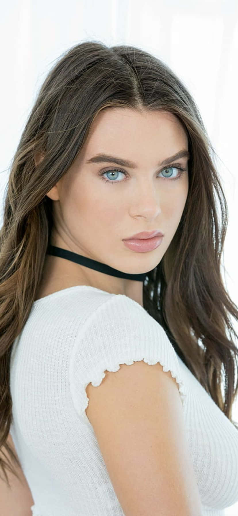  壁紙 — 一位擁有引人注目的藍色眼睛和長棕色頭髮的女性，在明亮的白色背景前穿著白色羅紋上衣和黑色頸鏈。