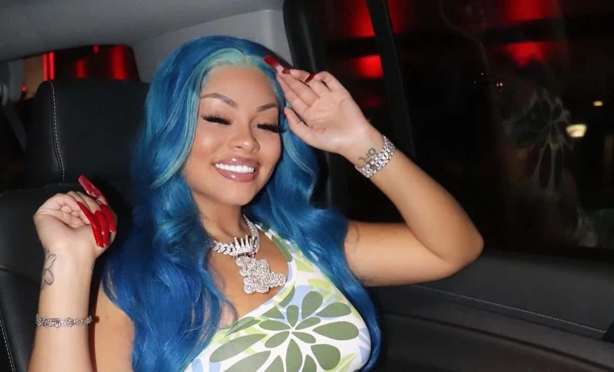  壁紙 — 一位擁有充滿活力的藍色頭髮的女性坐在紅色氛圍燈光的車內微笑。