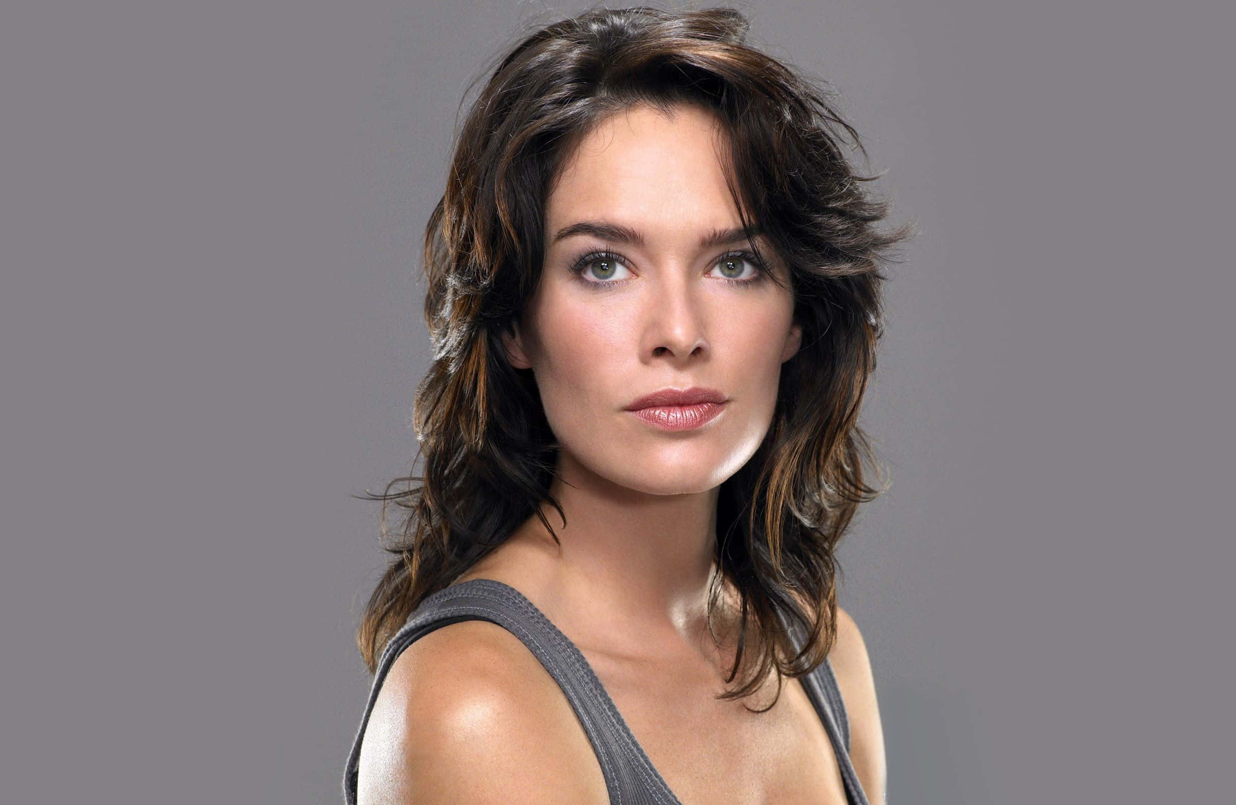Lena Headey 桌布 壁紙 — 一位擁有波浪形棕色頭髮和綠色眼睛的女性，在純灰色背景下直視鏡頭。
