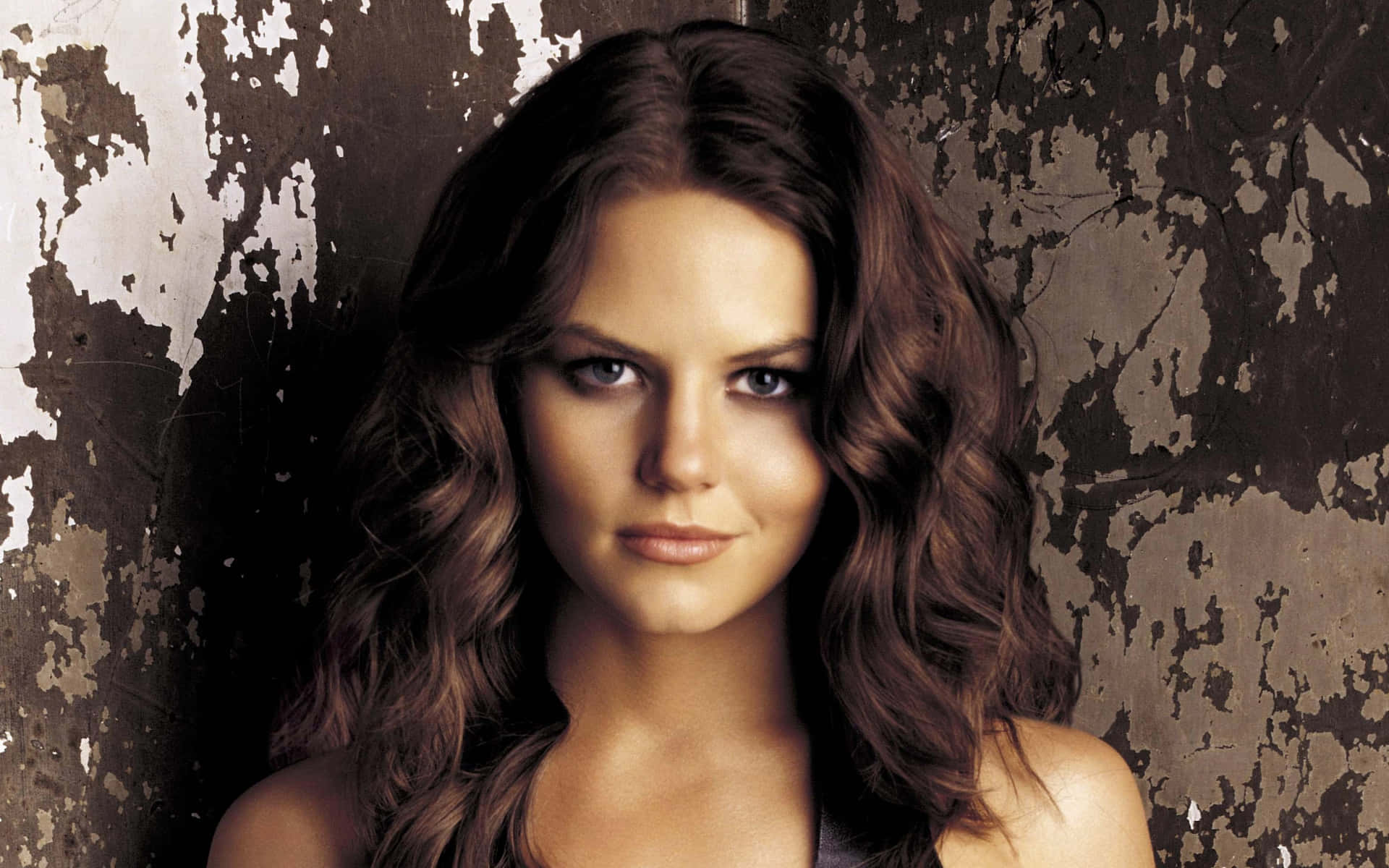 jennifer morrison 桌布 壁紙 — 一位擁有波浪棕色頭髮的女性，在紋理剝落的牆壁背景下直視鏡頭。