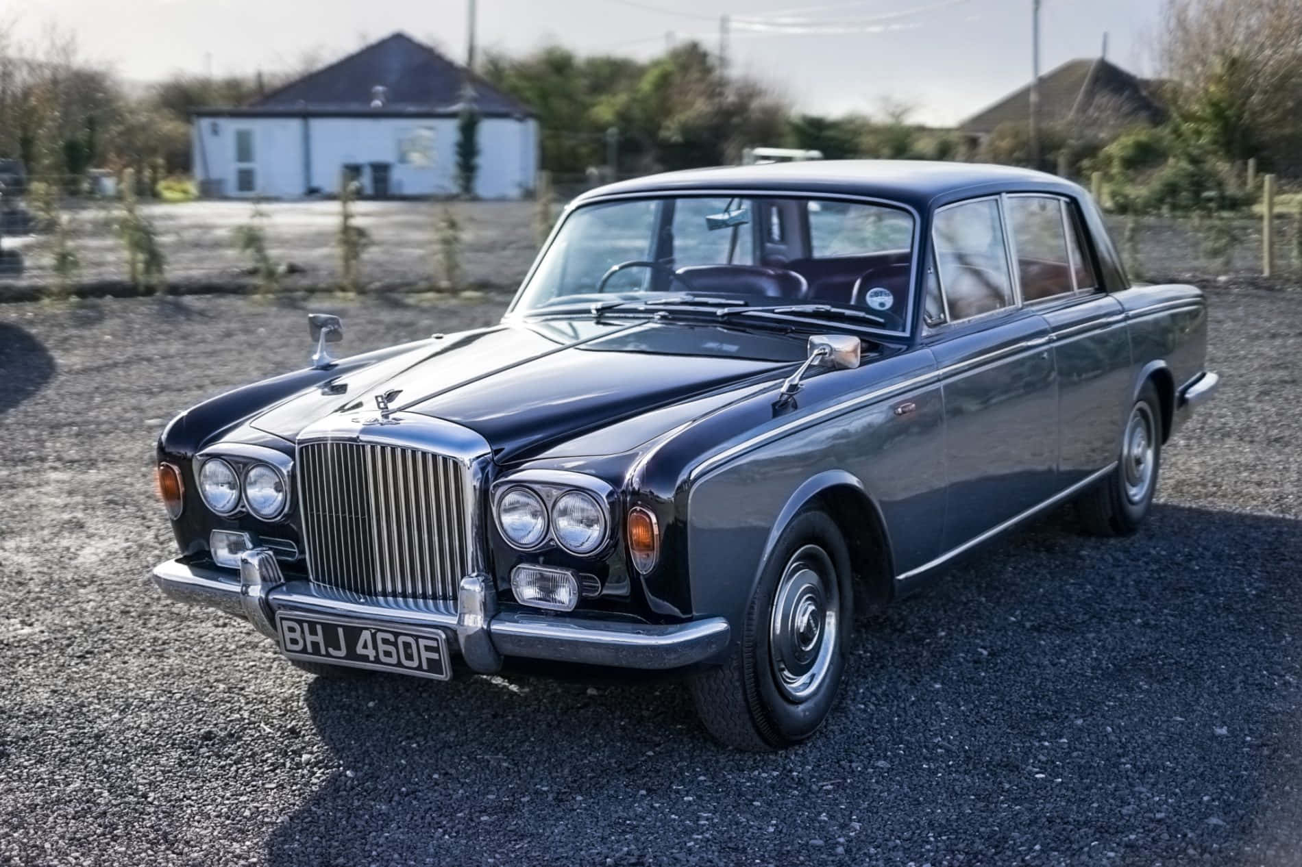 Bentley T1 桌布 壁紙 — 一台時尚的黑色復古賓利轎車在明亮的陽光下閃閃發光，停在碎石地上，背景是一座白色房子。