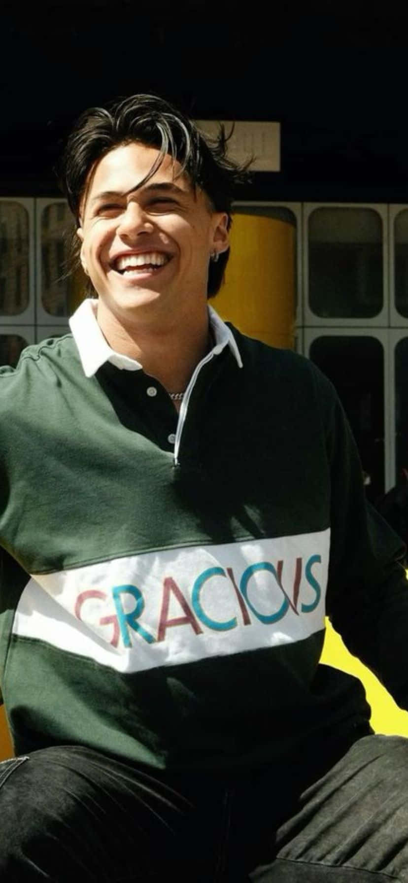  壁紙 — 一位黑髮年輕男子穿著帶有彩色「GRACIOUS」條紋的綠色Polo衫，開懷大笑。