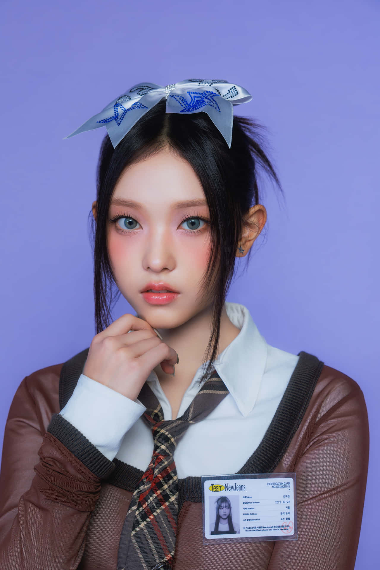 壁紙 — 一位身穿校服、佩戴藍色蝴蝶結和識別證徽章的年輕女性，在純紫色背景前擺姿勢。