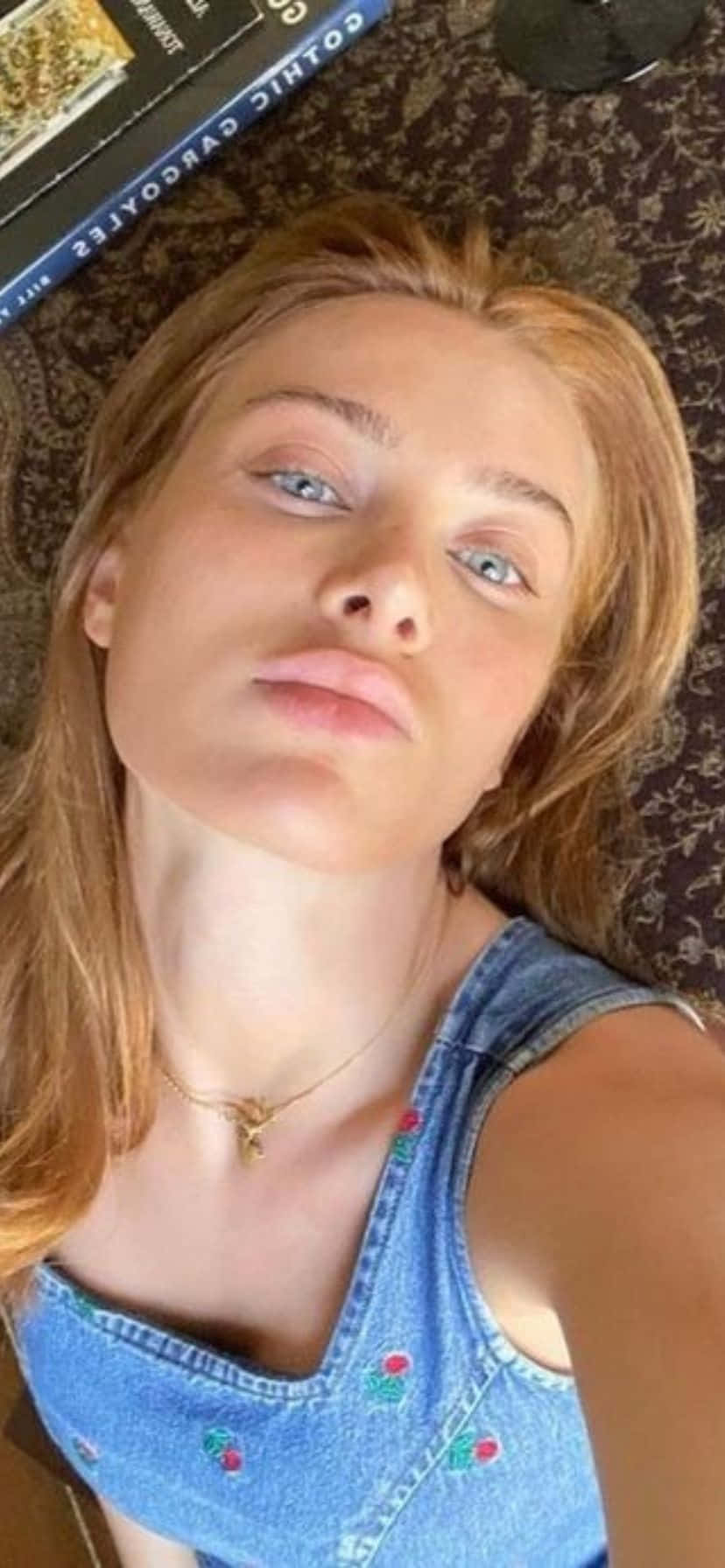  壁紙 — 一位金髮藍眼的年輕女性躺在圖案地毯上，身穿牛仔上衣和金色項鍊。