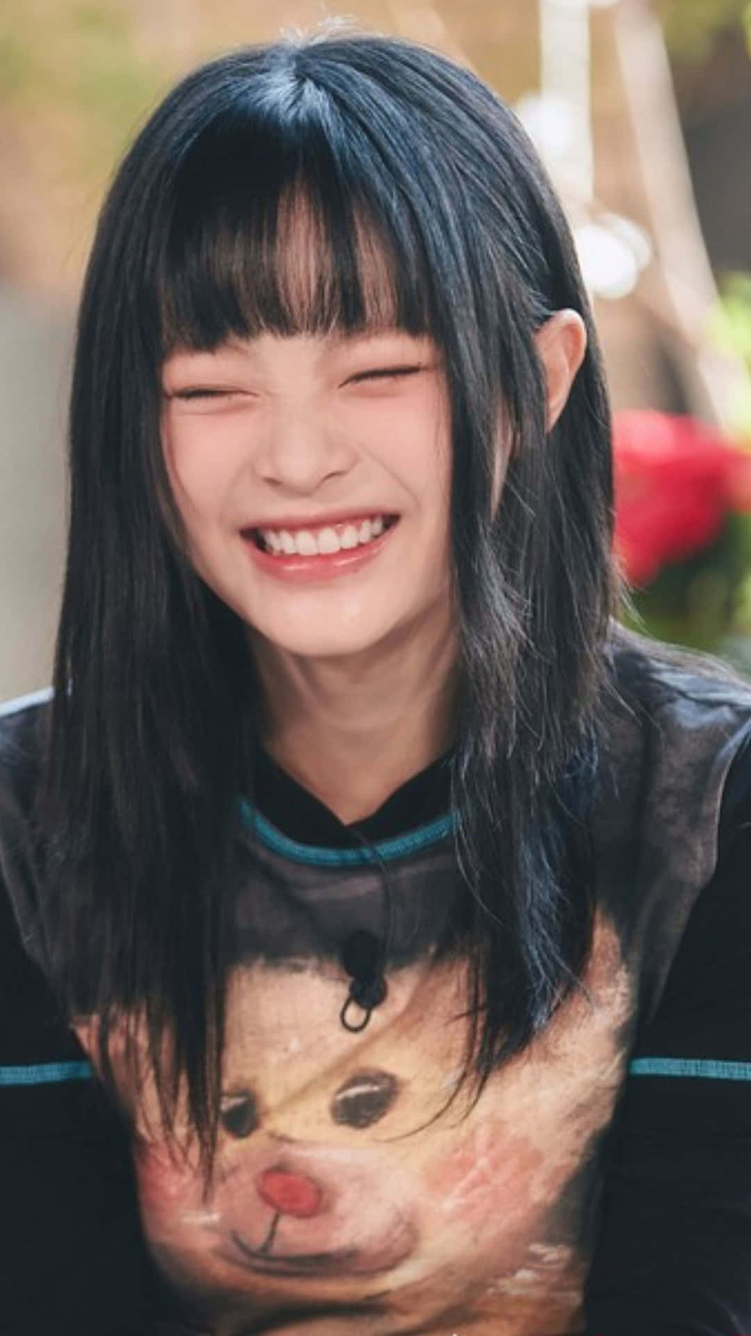  壁紙 — 一位黑髮年輕女性穿著帶有泰迪熊圖案的襯衫，開心地笑著。