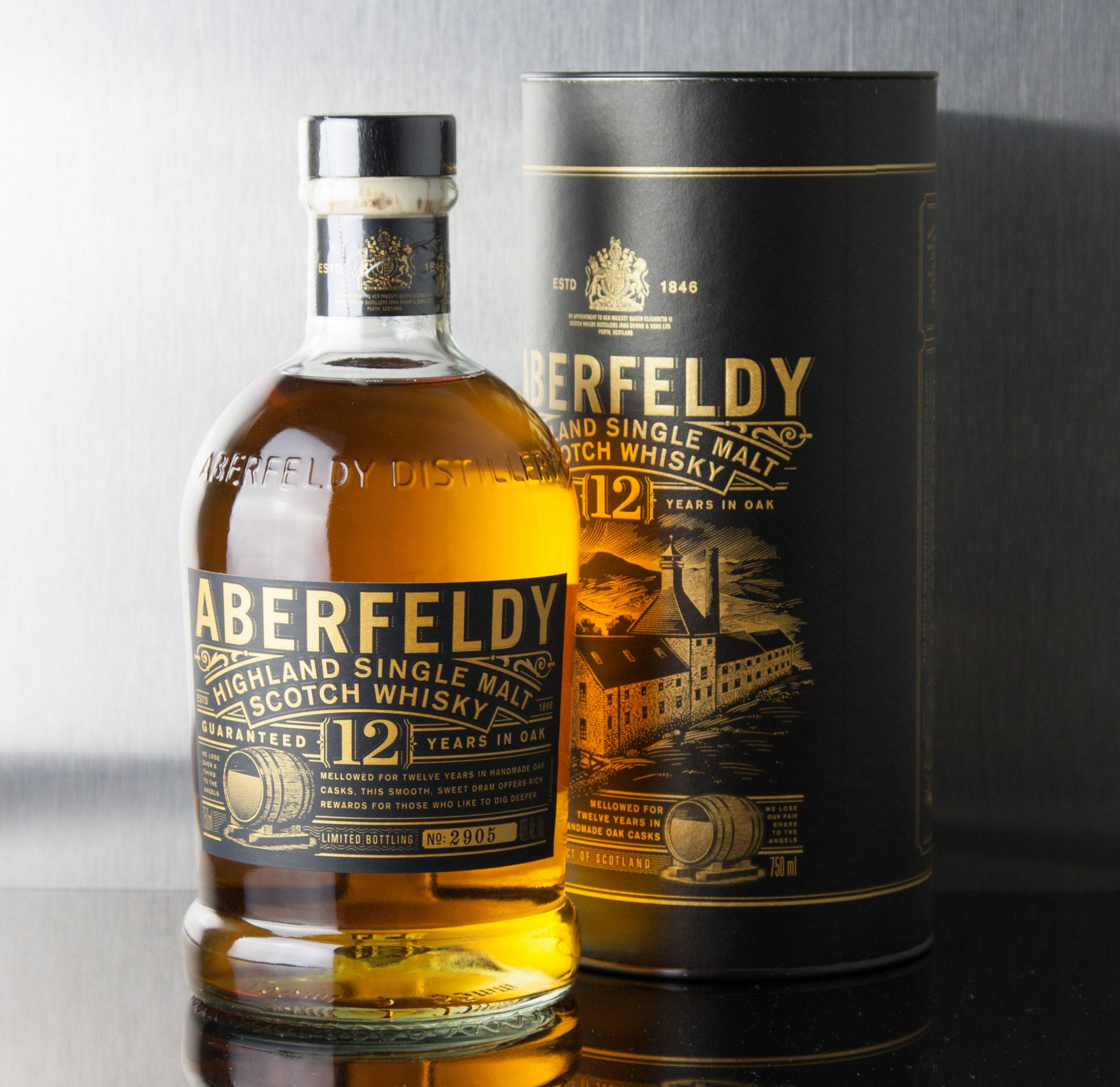 Drink 桌布 壁紙 — Aberfeldy 12年高地單一麥芽蘇格蘭威士忌酒瓶和帶有金箔細節的圓柱形盒子，放置在反射黑色表面上，背景為拉絲金屬。