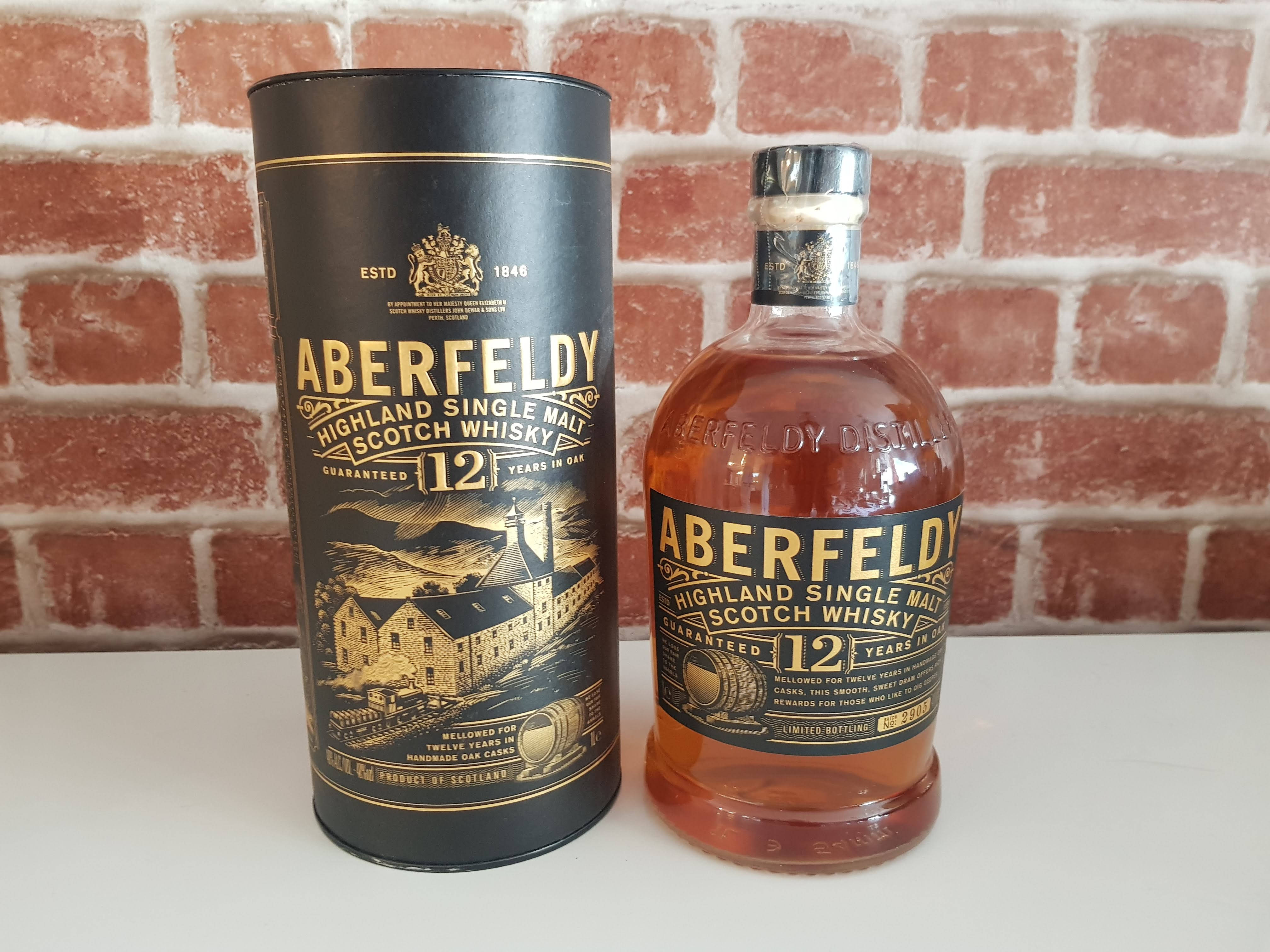 飲料 桌布 壁紙 — Aberfeldy 12年高地單一麥芽蘇格蘭威士忌酒瓶和禮盒，放在白色表面上，背景是紅磚牆。