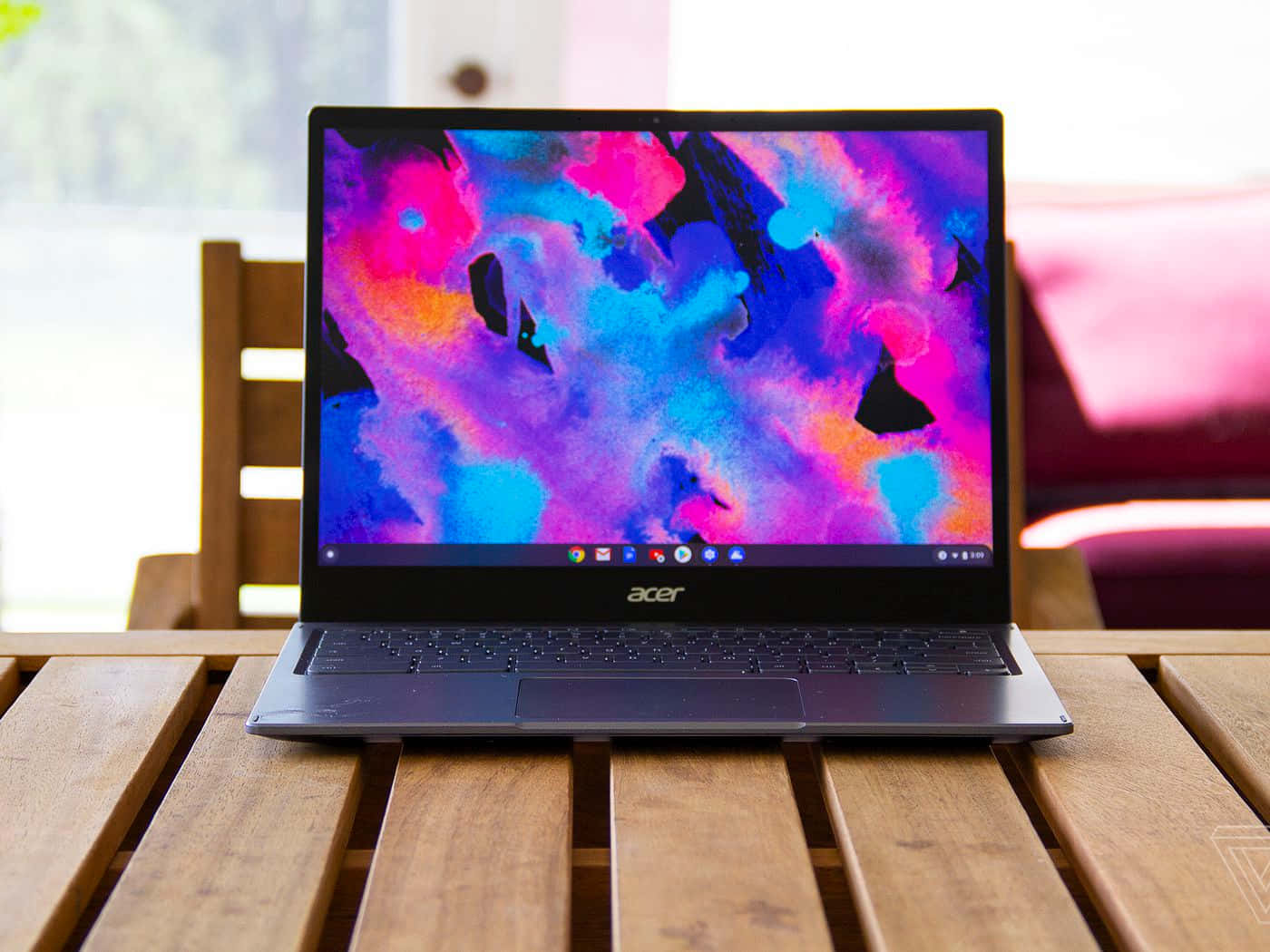 Chromebook 桌布 壁紙 — Acer 筆記型電腦帶有鮮豔的抽象桌布，打開放在窗邊的木條桌上。