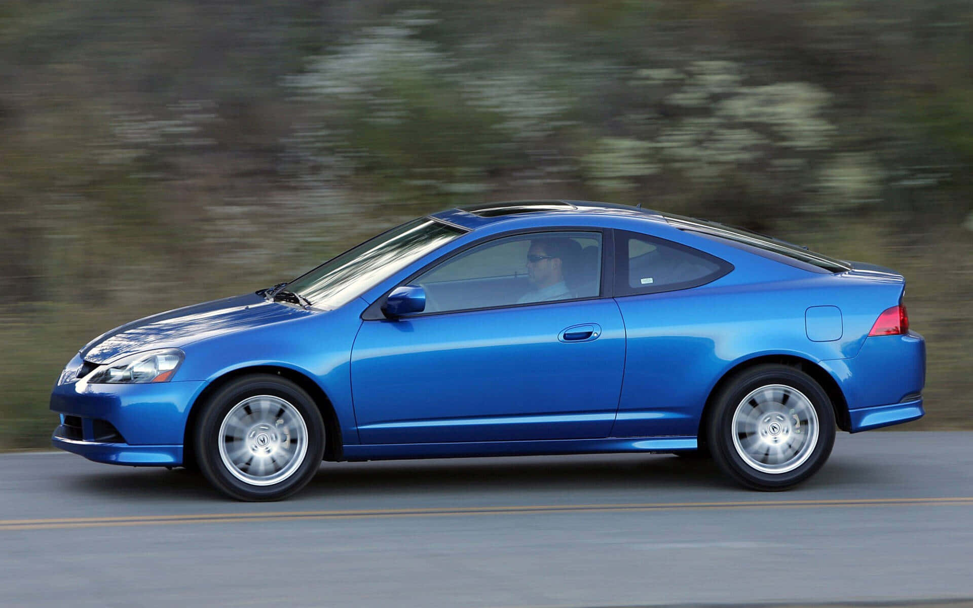 Acura RSX：性能與奢華的完美結合 壁紙 — 一輛充滿活力的藍色運動型轎跑車在道路上疾馳，背景是模糊的綠色植物。