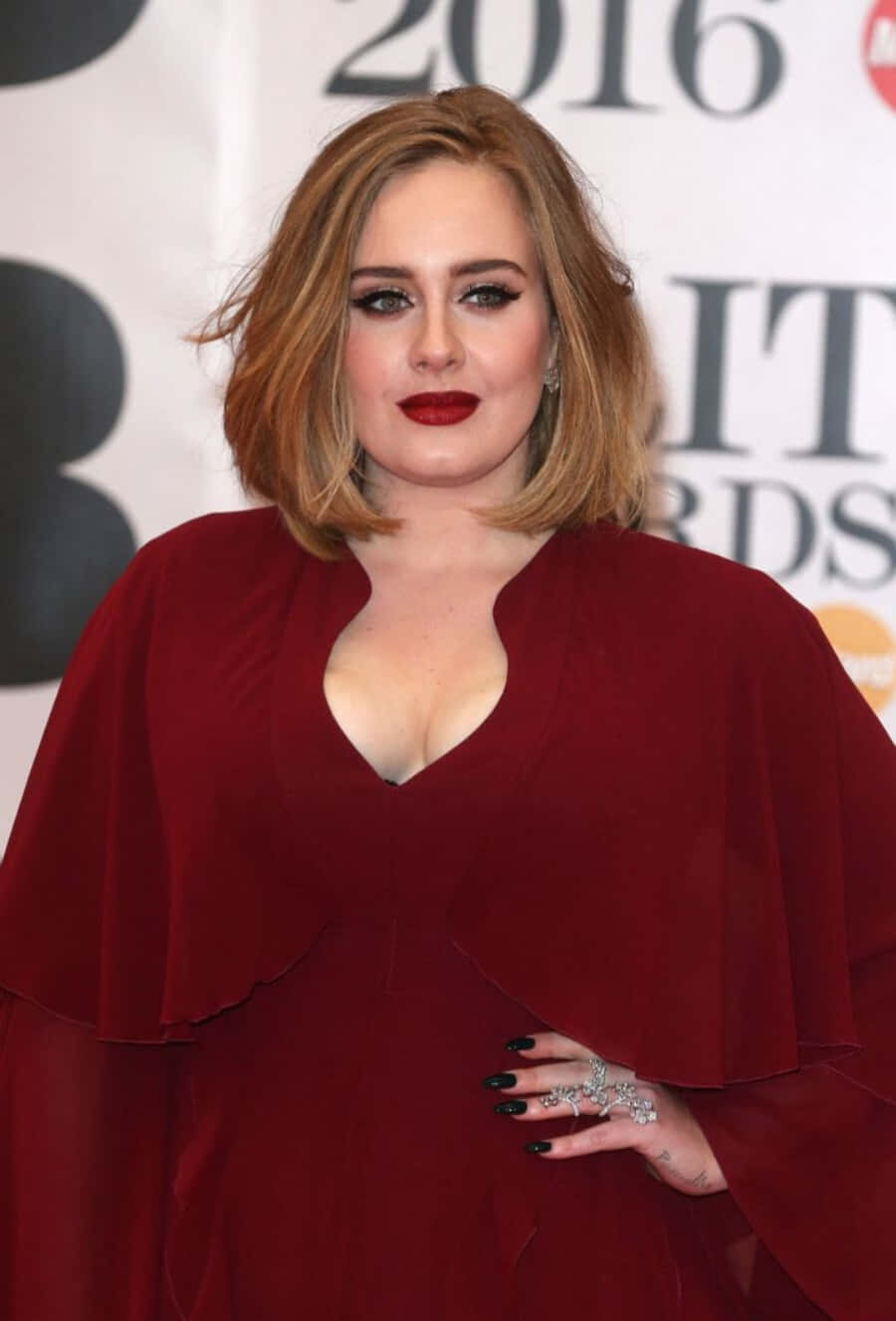 愛黛兒 桌布 壁紙 — Adele 在2016年全英音樂獎上自信地穿著深紅色斗篷裙，搭配大膽的紅色唇膏和黑色指甲油。