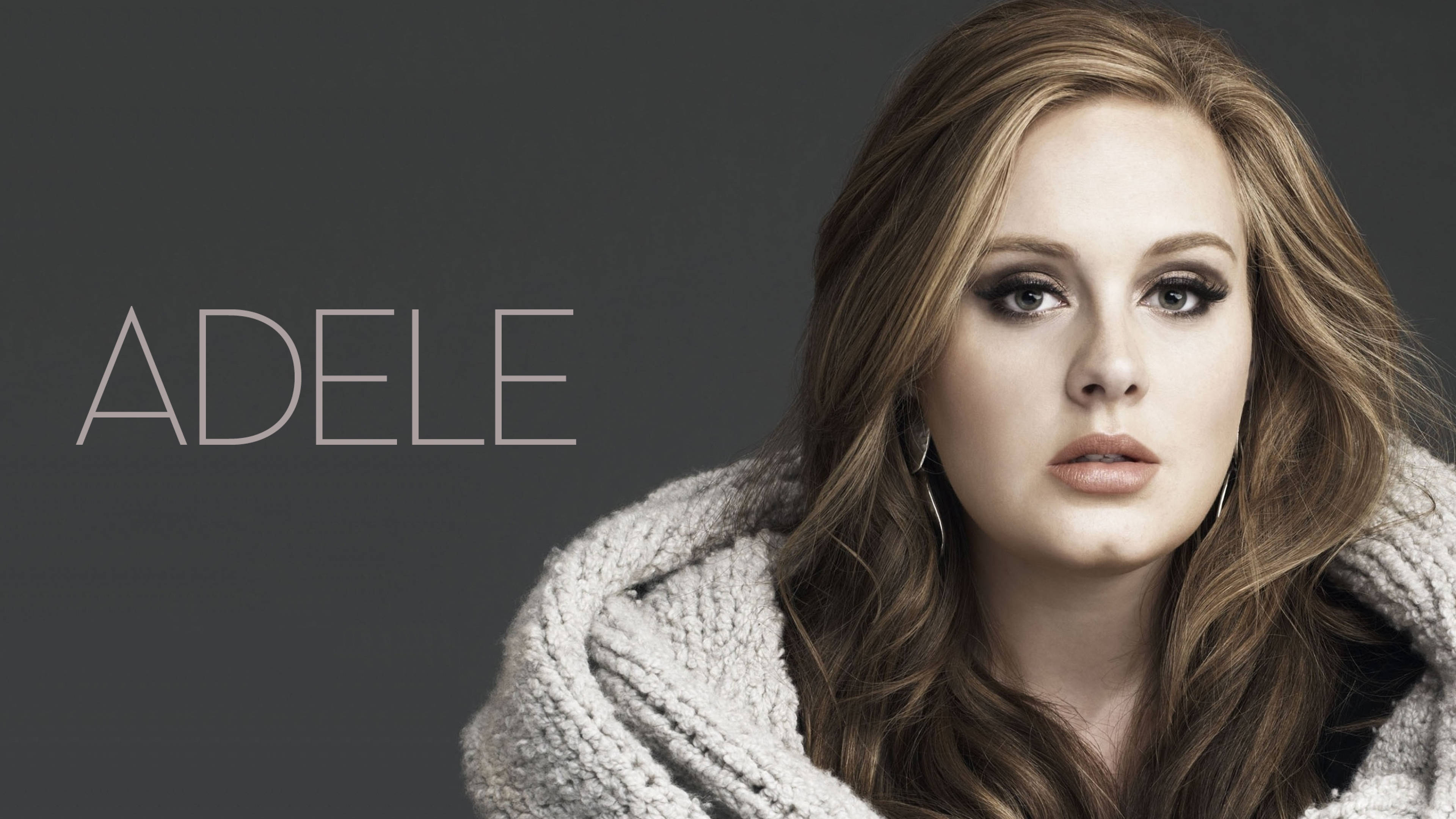 Adele 桌布 壁紙 — Adele 穿著質感灰色針織毛衣，在柔和灰色背景前凝視鏡頭，旁邊以極簡字體顯示她的名字。