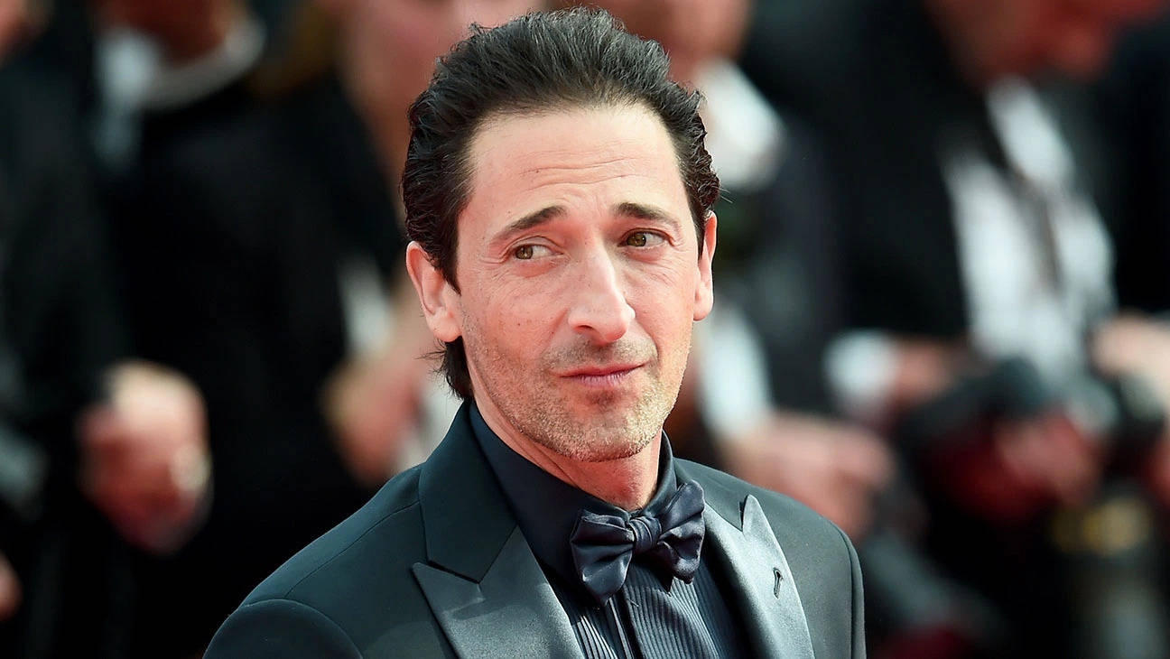 Adrien 桌布 壁紙 — Adrien Brody 身穿黑色燕尾服配蝴蝶結，在紅地毯上若有所思地凝視鏡頭，身後是模糊的人群。