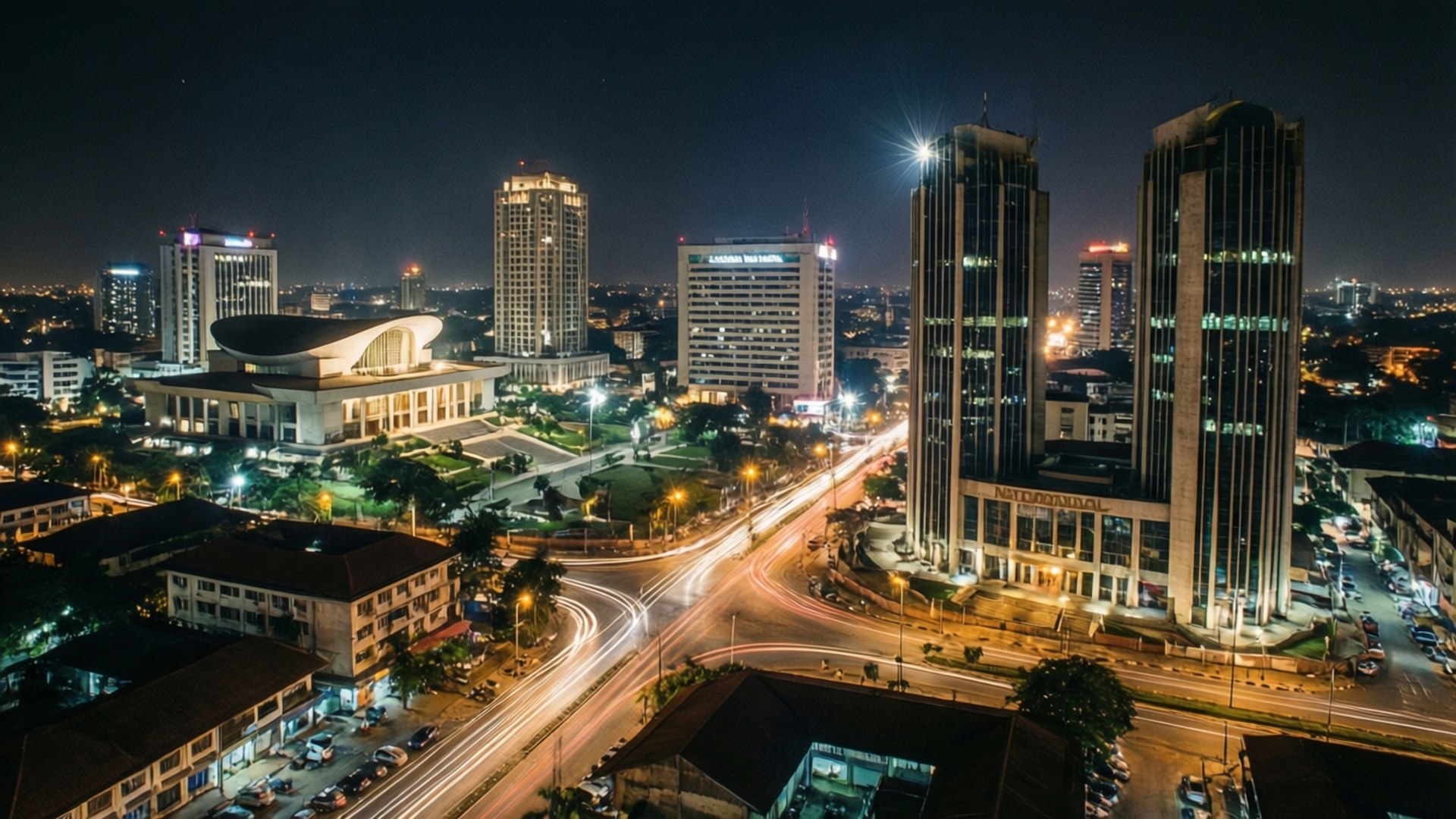 Accra Night Skyline 壁紙 — 繁忙城市景觀的空中夜景，有明亮的摩天大樓和交通發出的發光光跡。