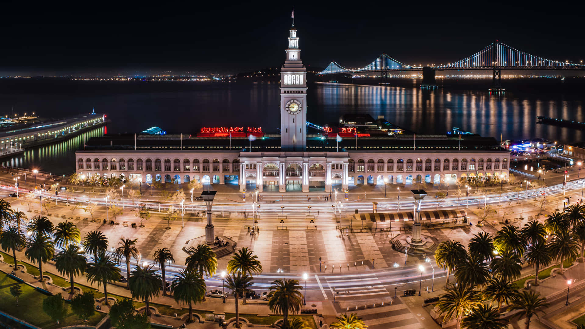  壁紙 — 渡輪大廈的夜間空中景觀，閃爍的燈光倒映在水面上，背景是海灣大橋。