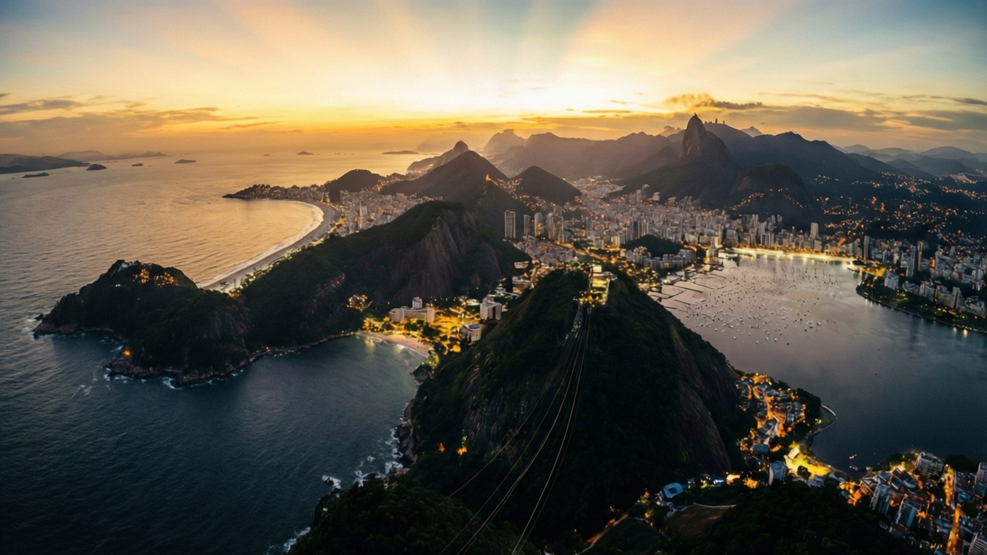 Rio Coastline Golden Hour 壁紙 — 里約熱內盧的空中日落景觀，糖麵包山的纜車在金色天空和海洋的映襯下閃閃發光。