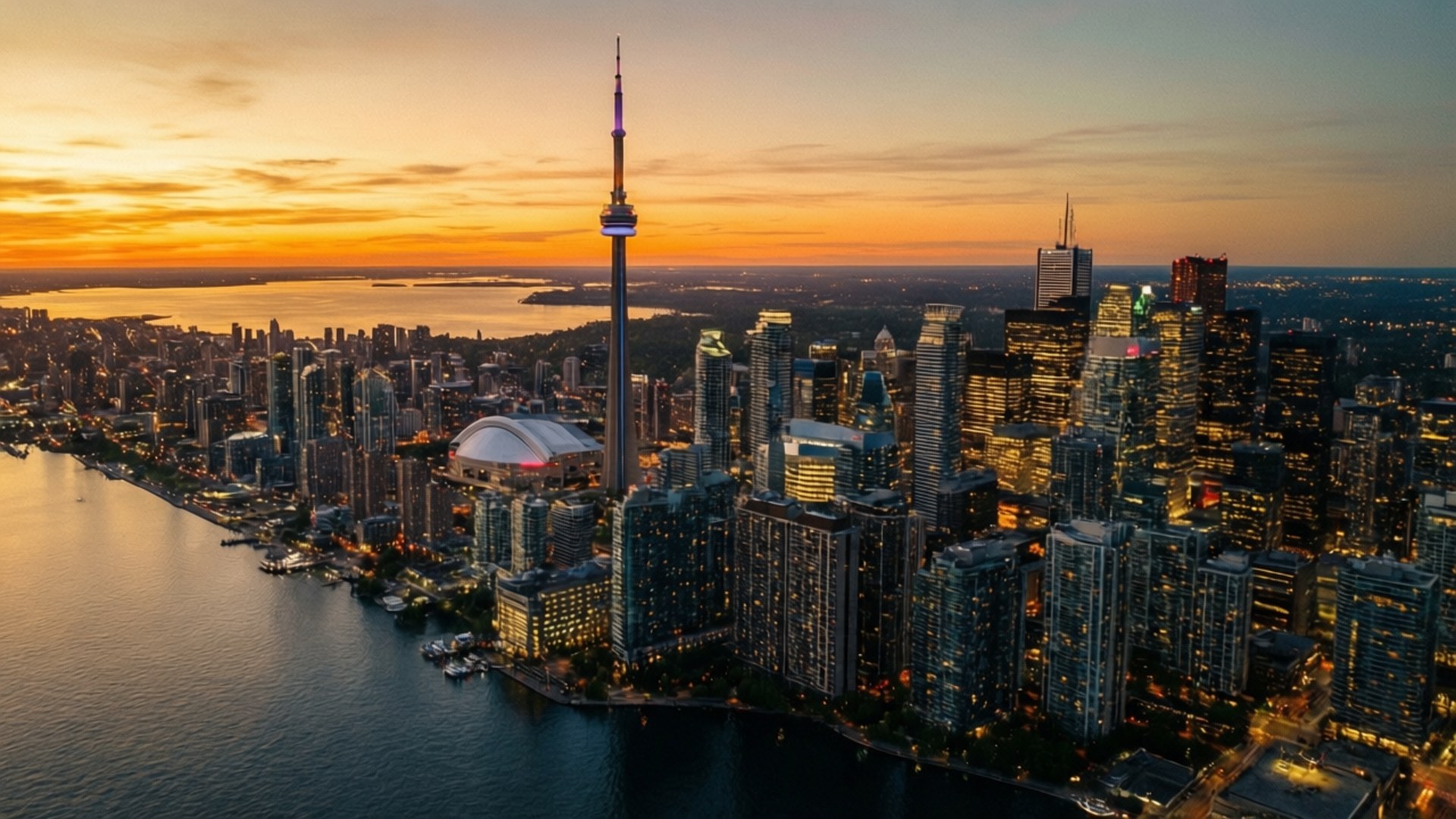 Toronto Sunset Skyline 壁紙 — 多倫多天際線的日落空中景觀，CN 塔在橙色天空下閃耀，海濱城市燈光倒映在水面上。