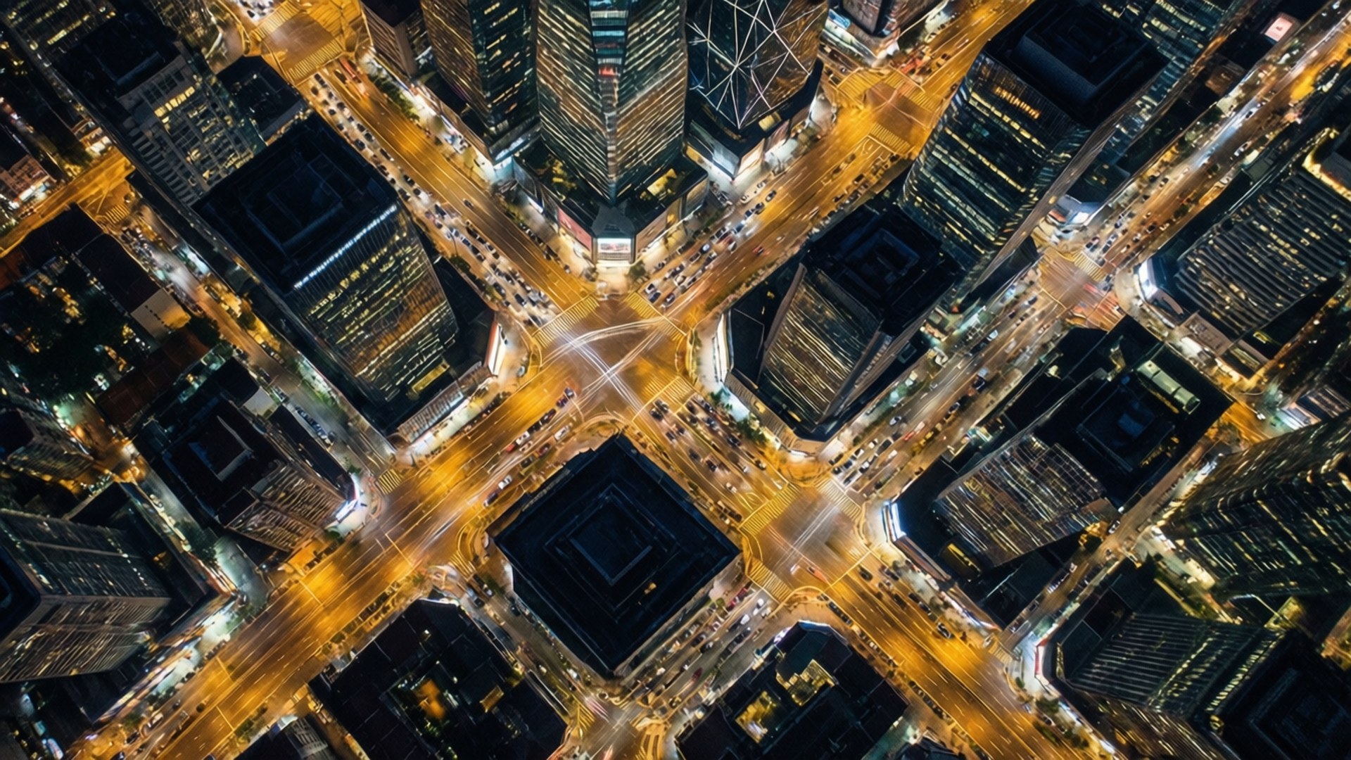 Aerial City Grid 壁紙 — 夜晚繁忙城市交叉口的鳥瞰圖，帶有發光的黃色路燈和高聳的摩天大樓。