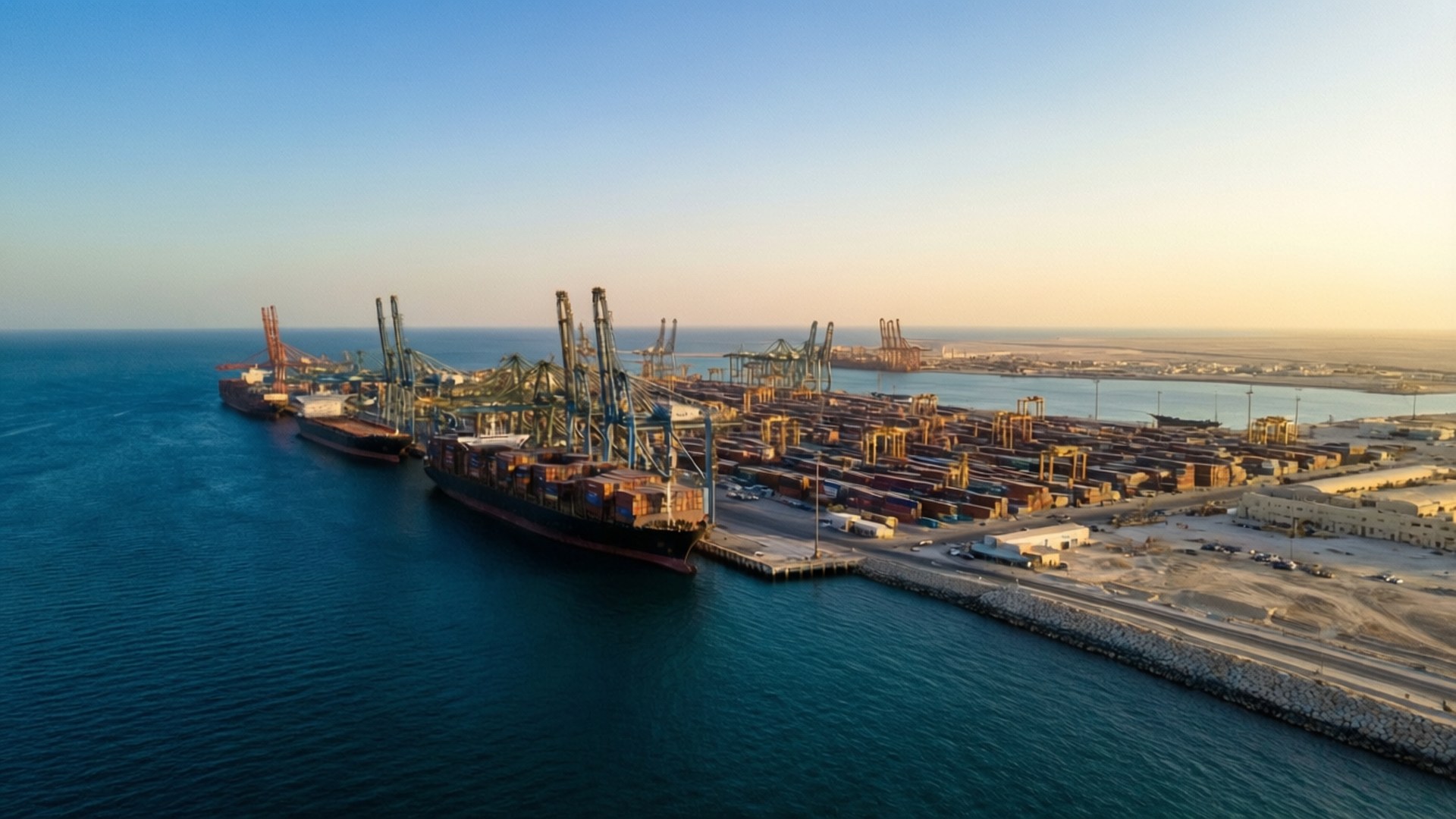 Gwadar Port Sunrise 壁紙 — 日落時分繁忙港口的鳥瞰圖，巨大的貨櫃船停泊在高聳的起重機和色彩繽紛的貨櫃堆旁邊。