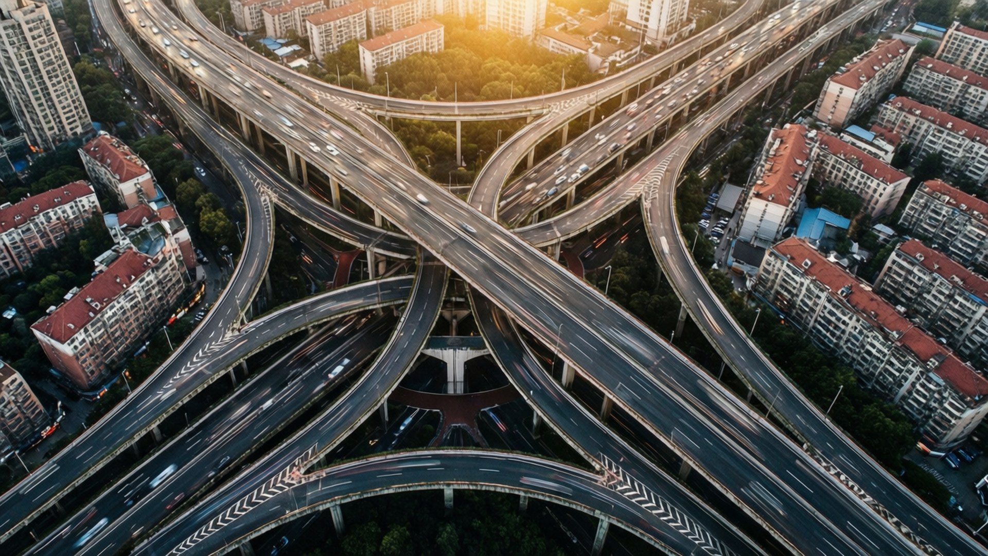 Highway Interchange 壁紙 — 黃金時段複雜高速公路交匯處的鳥瞰圖，汽車穿過分層高架橋，周圍環繞著城市建築和樹木。