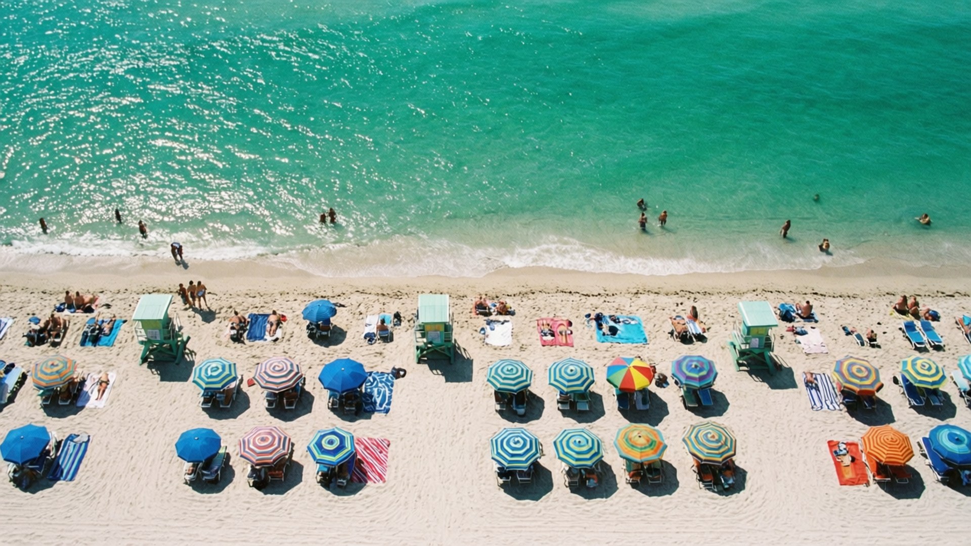 Beach Day Pattern 壁紙 — 俯瞰擠滿人群的海灘，色彩繽紛的遮陽傘和人們在毛巾上放鬆，靠近碧綠的海水。
