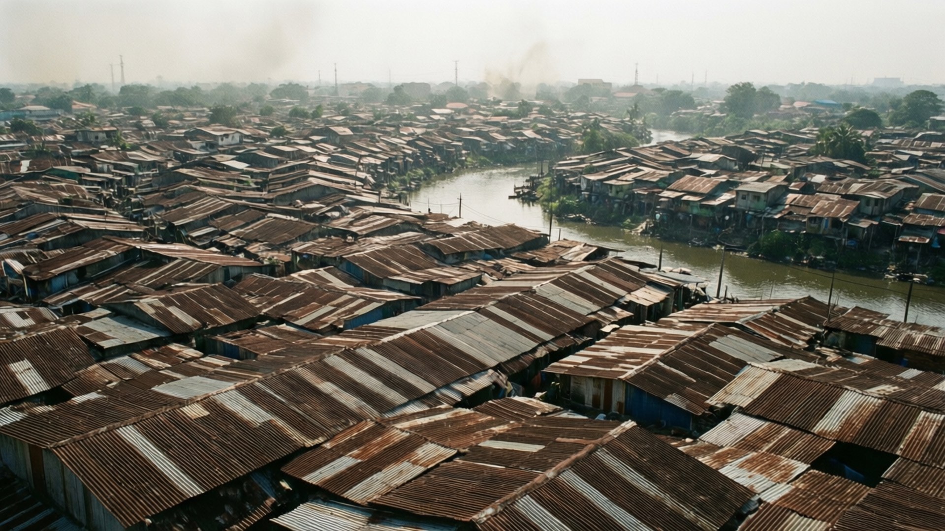 Kampung Bayur Aerial 壁紙 — 密集城市聚居地的鳥瞰圖，有生鏽的波紋鐵皮屋頂和一條蜿蜒的河流穿過貧民窟。