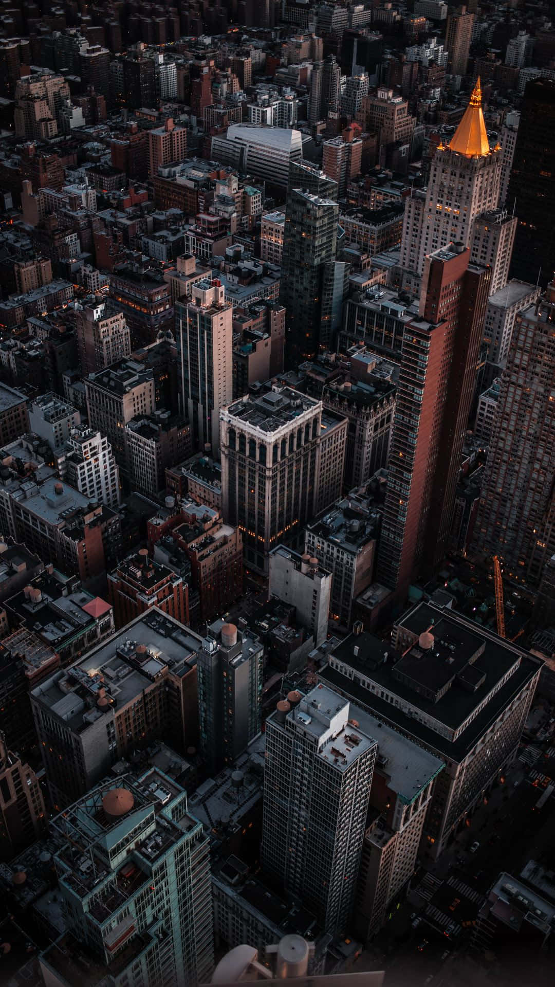 黃昏時分密集城市的鳥瞰圖，金色尖塔在黑暗建築物上方發光。 — 城市 壁紙