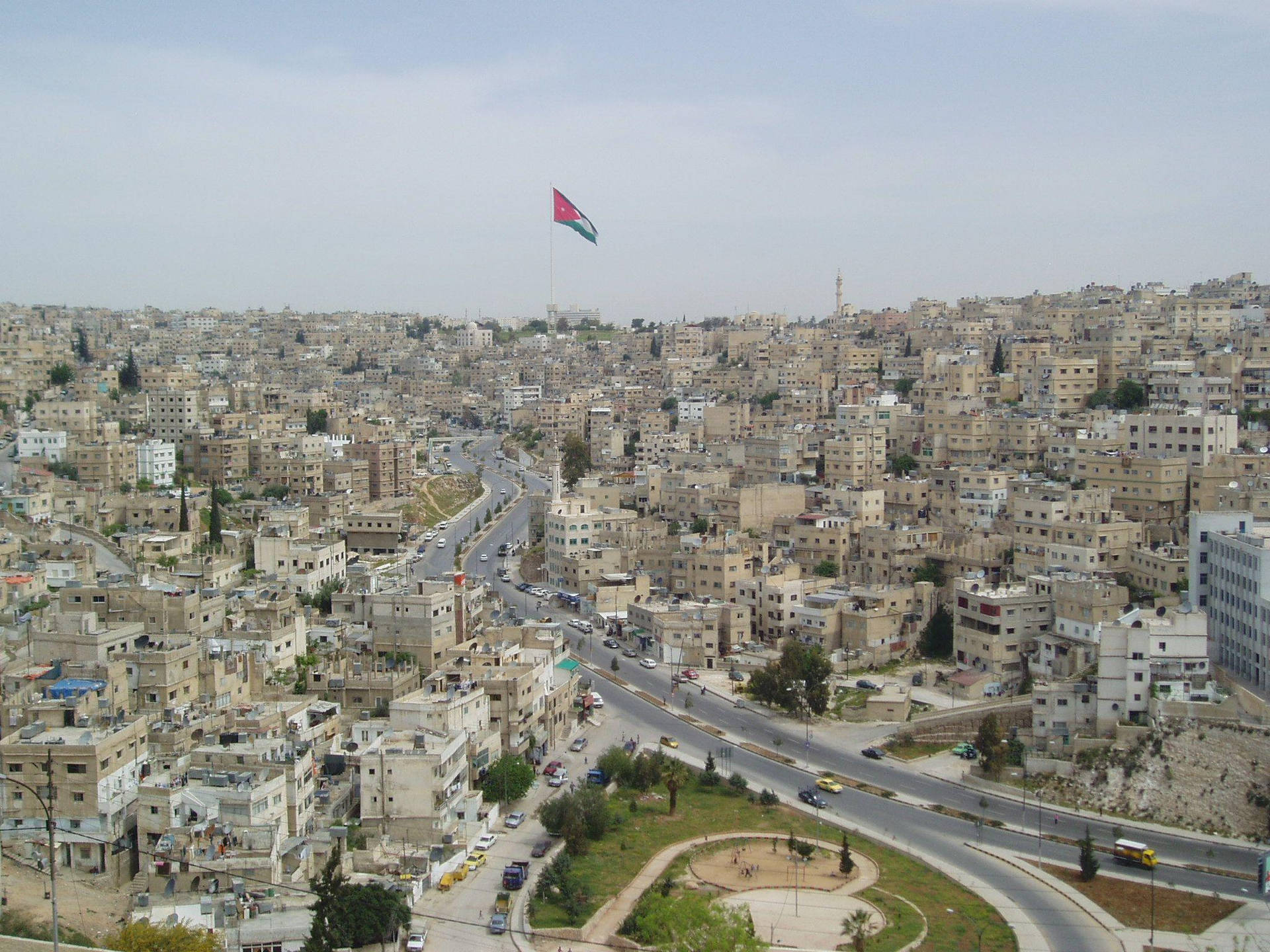 從空中俯瞰米色城市，有道路和山頂上飄揚的旗幟。 — Jordan 壁紙