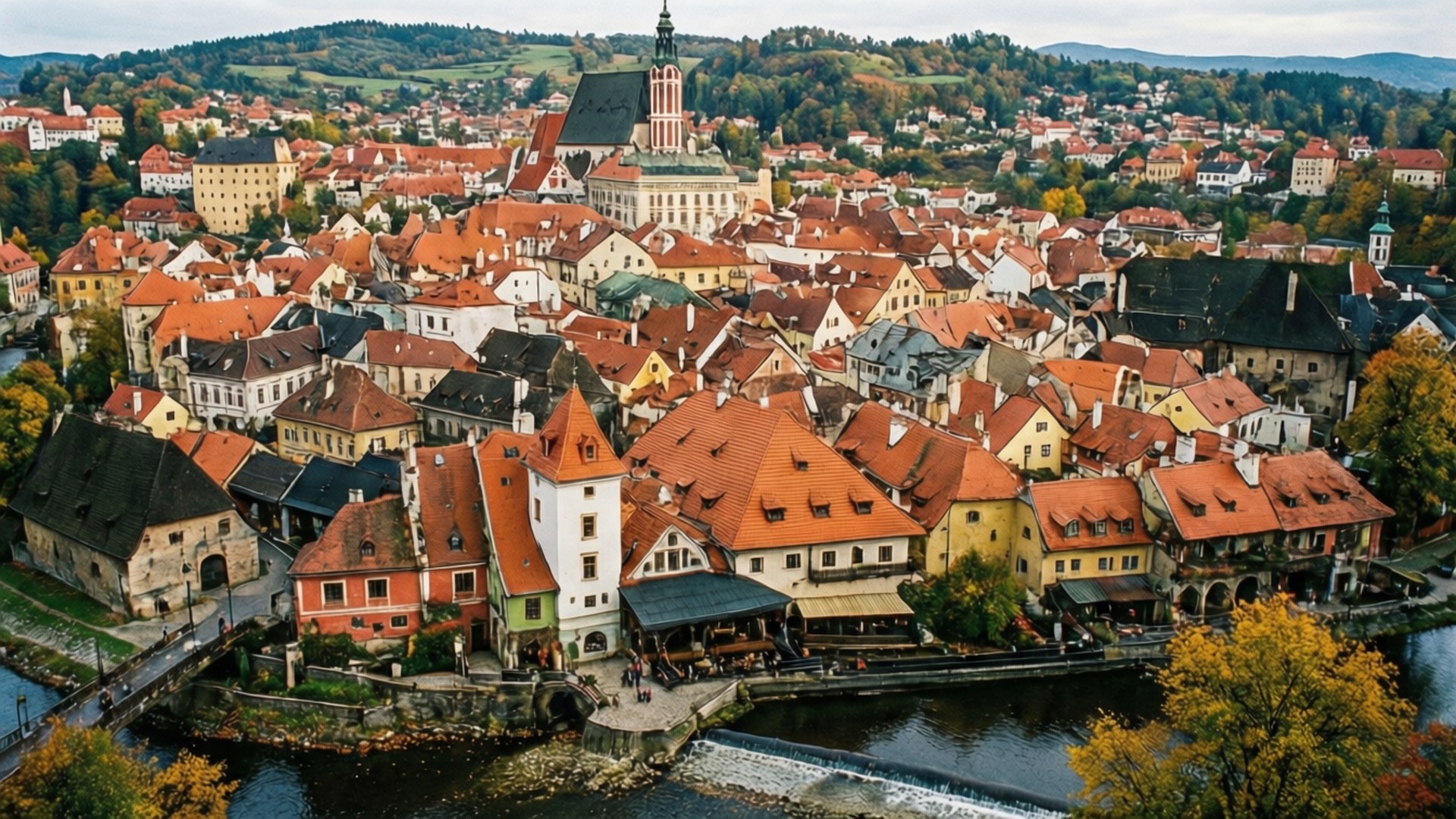 Český Krumlov Panorama 壁紙 — 歷史悠久的歐洲小鎮的鳥瞰圖，擁有紅色瓦片屋頂，坐落在河邊，秋葉繽紛。