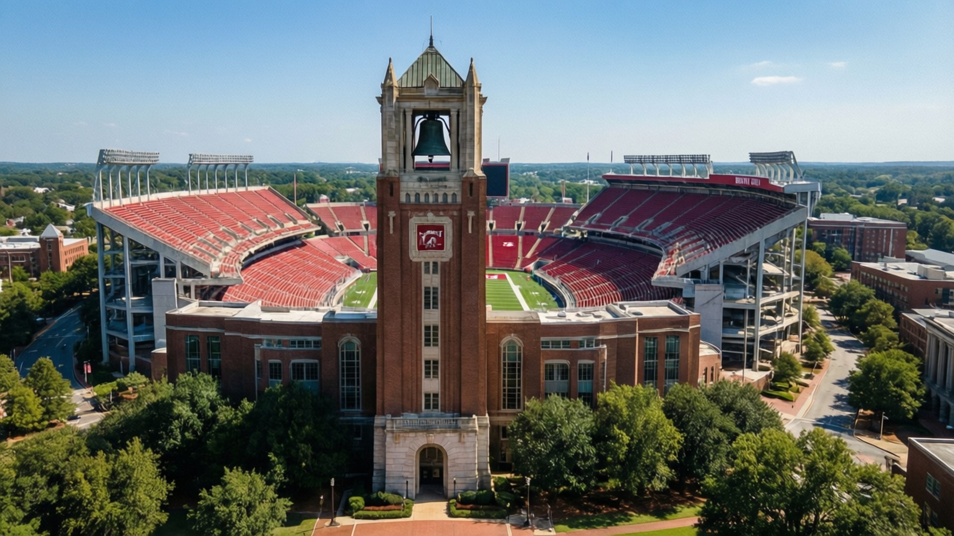 Alabama University Aerial 壁紙 — 大型體育館的鳥瞰圖，設有紅色座位和中央磚砌鐘樓，鐘樓上有可見的鐘，在晴朗的藍天下。
