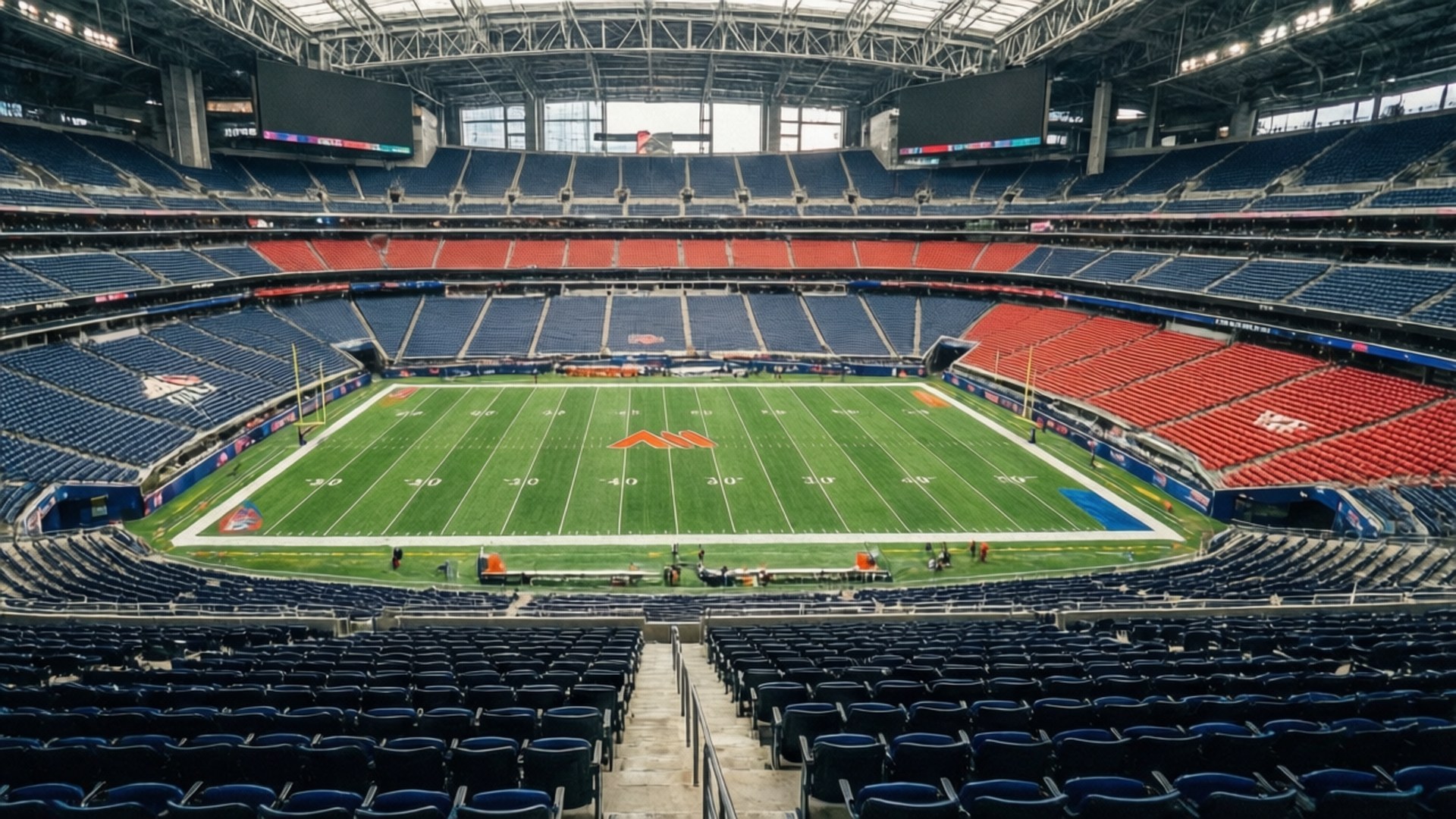 Stadium Architecture 壁紙 — 鋼鐵屋頂下一個巨大空足球場的鳥瞰圖，擁有充滿活力的綠色場地和藍紅座位。