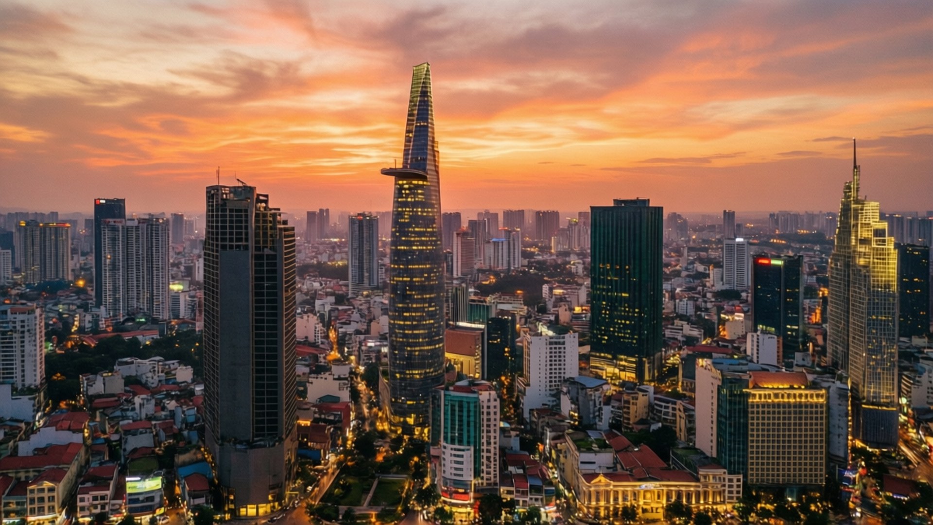 Sunset Skyline Panorama 壁紙 — 現代城市天際線的鳥瞰圖，夕陽西下，橙色雲彩和燈火輝煌的摩天大樓。